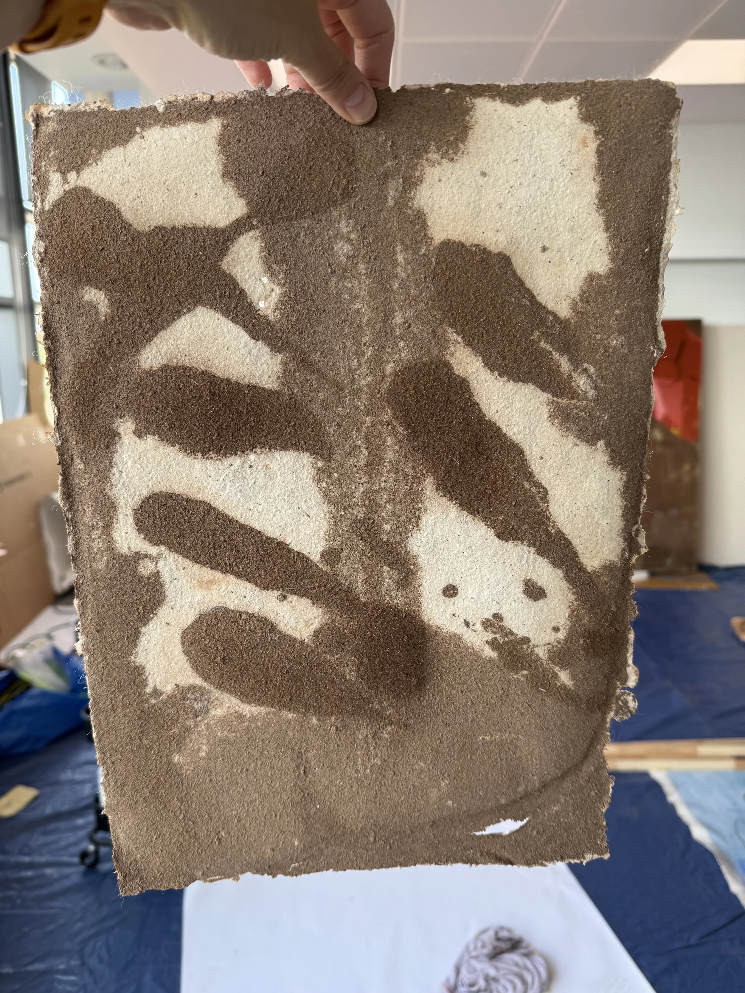 A person holding a piece of textured artwork that depicts a butterfly silhouette in earthy tones.