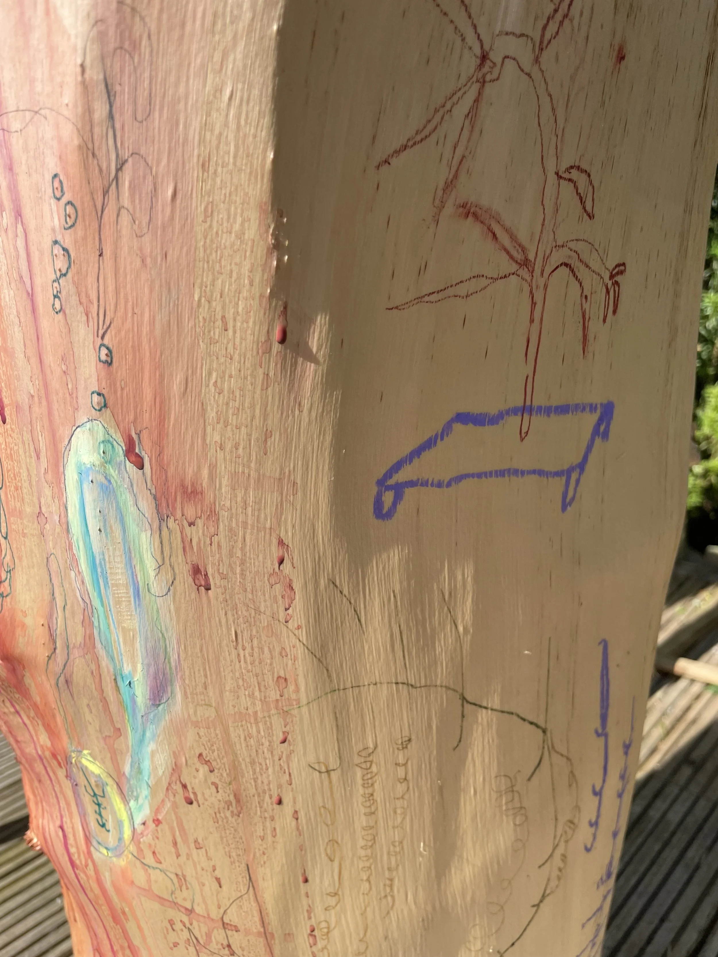 Wooden surface with colorful drawings and sketches, including a tree, a bench, and some abstract shapes.
