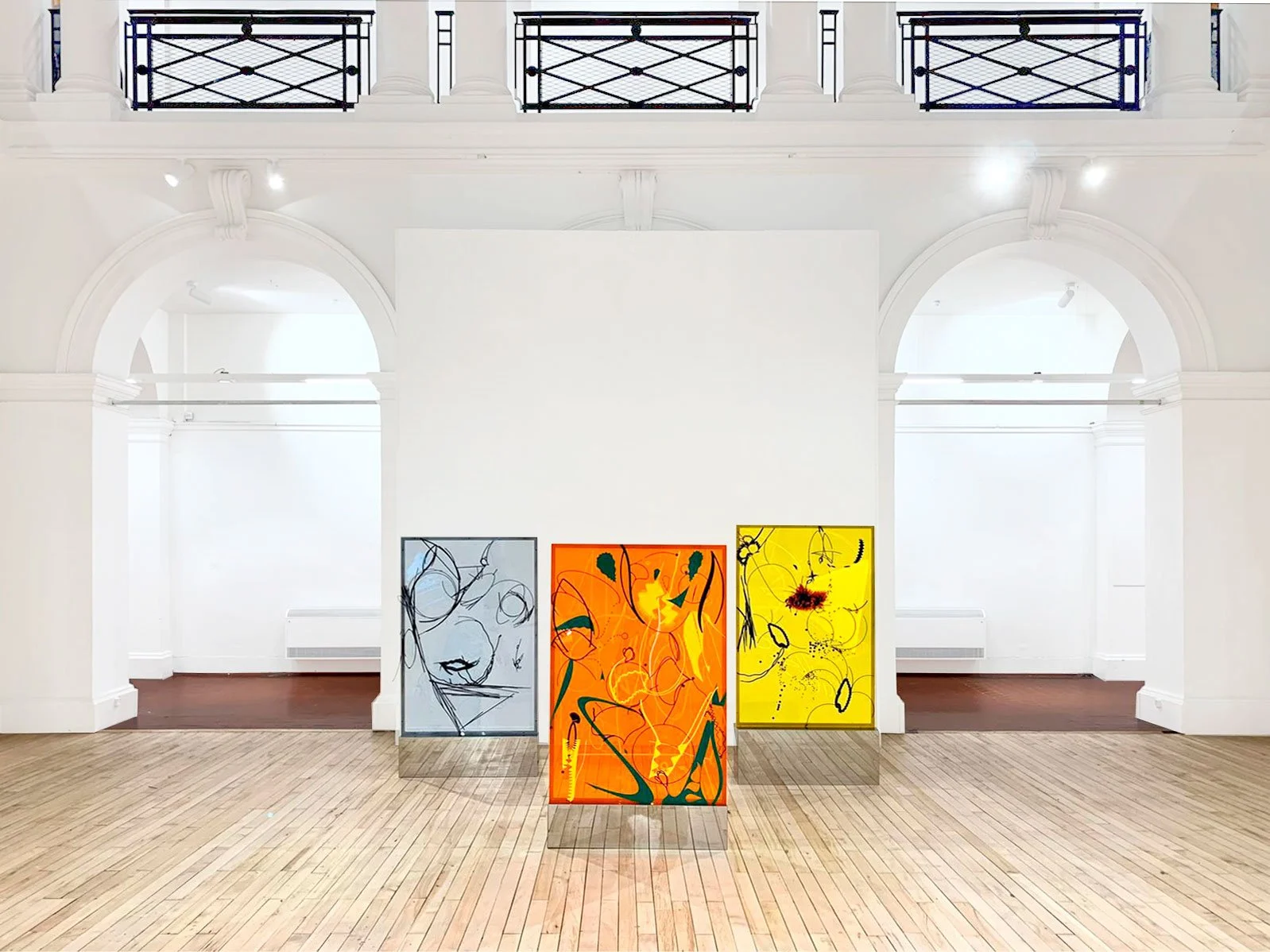 Three colorful abstract paintings on display in a bright art gallery with white walls and wooden floors.