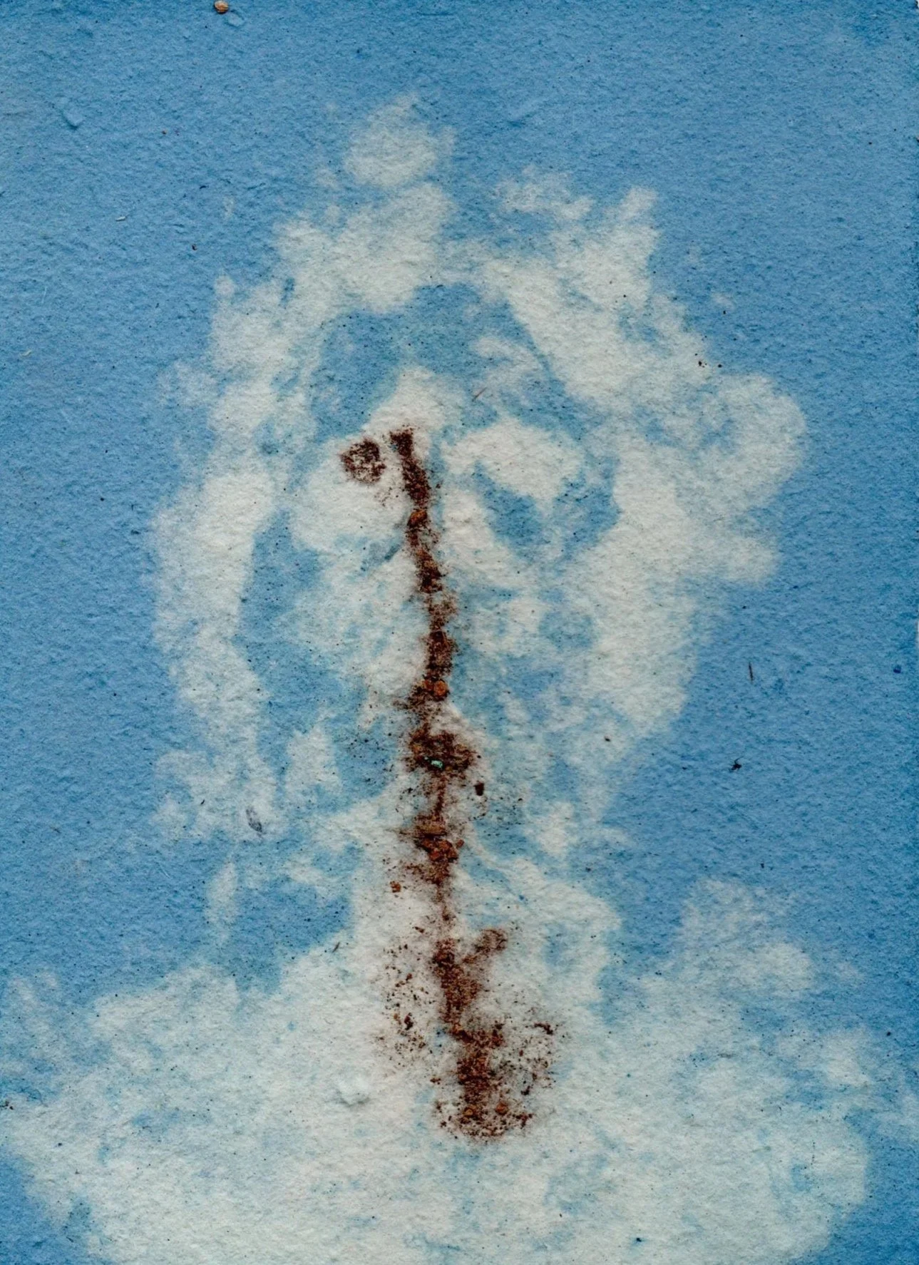 A cloud of white powder on a blue surface with a line of rust-colored powder running through the center, forming a shape resembling a face.