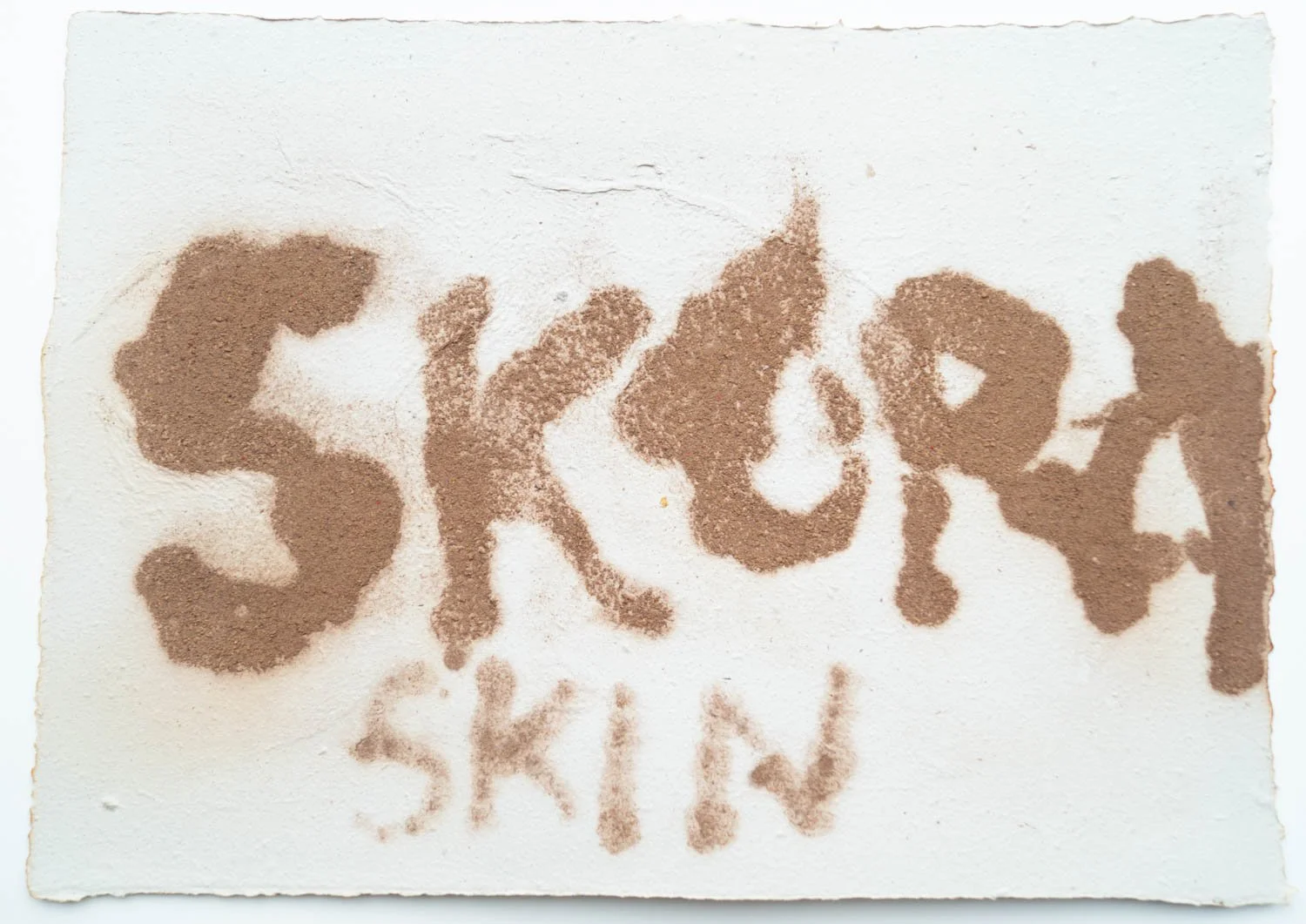Text written with cocoa powder on white paper reads 'SKIN' with some part of word unclear.
