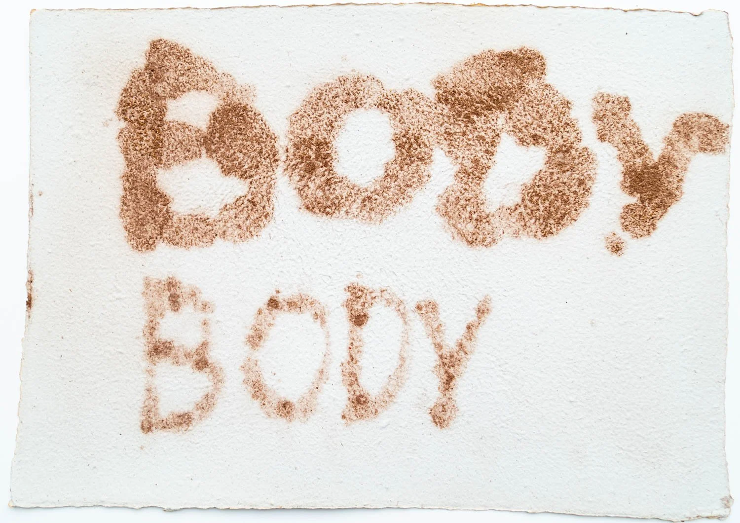 The words "Beefy" and "Body" are written on a piece of white paper using a brownish powder, possibly cocoa or cinnamon. The words are written in a casual, freehand style.
