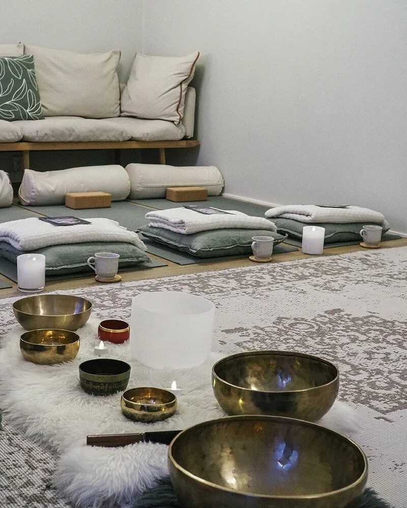 Äänimaljat lattialla, taustalla joogamatot, tyynyt ja viltit