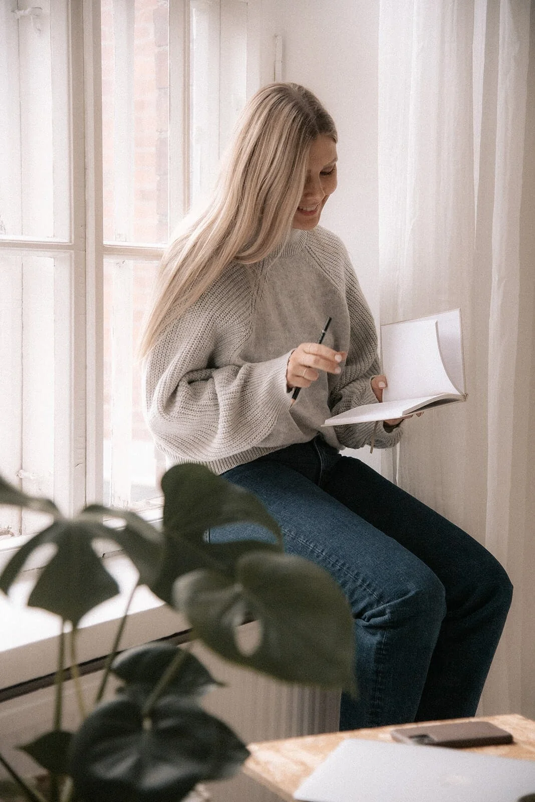 LCF Life Coach ratkaisukeskeinen valmentaja Terhi Lahti istuu ikkunalaudalla ja selaa muistikirjaa