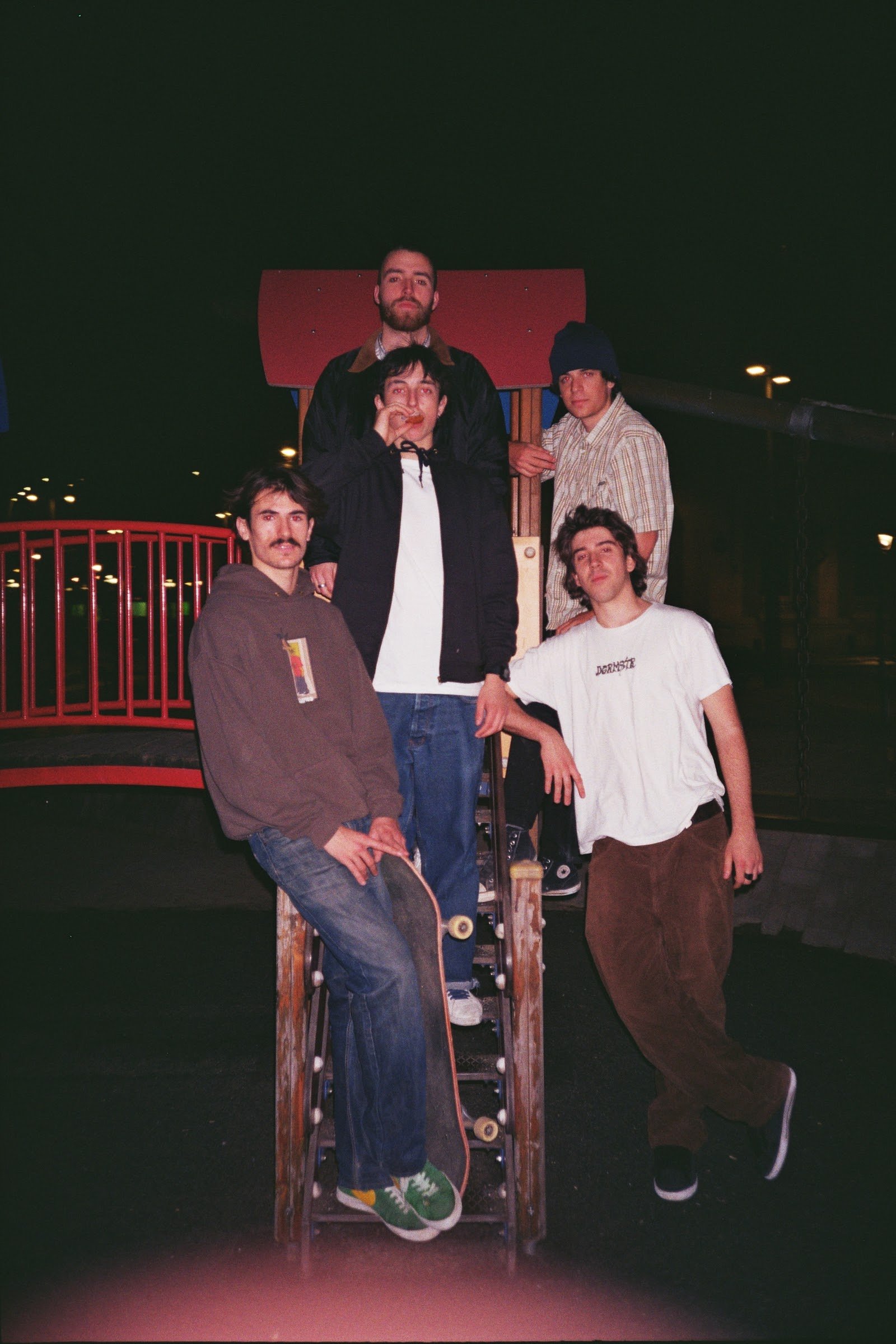Grupo de cinco jóvenes en un parque infantil en la noche, con estructuras de juego y ambiente oscuro.