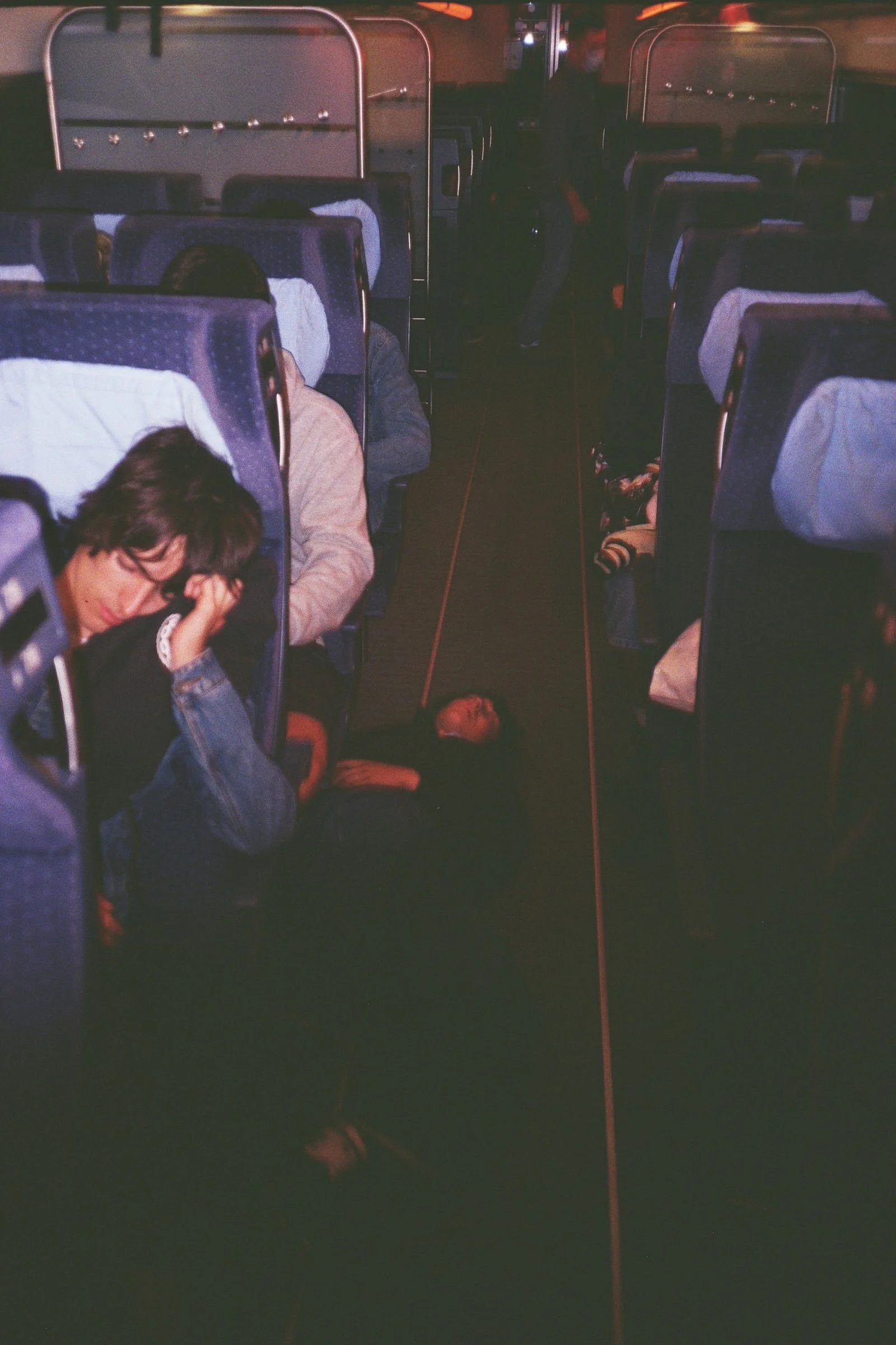 Una persona dormida en el pasillo de un autobús, rodeada de pasajeros durmiendo y ocupando los asientos.