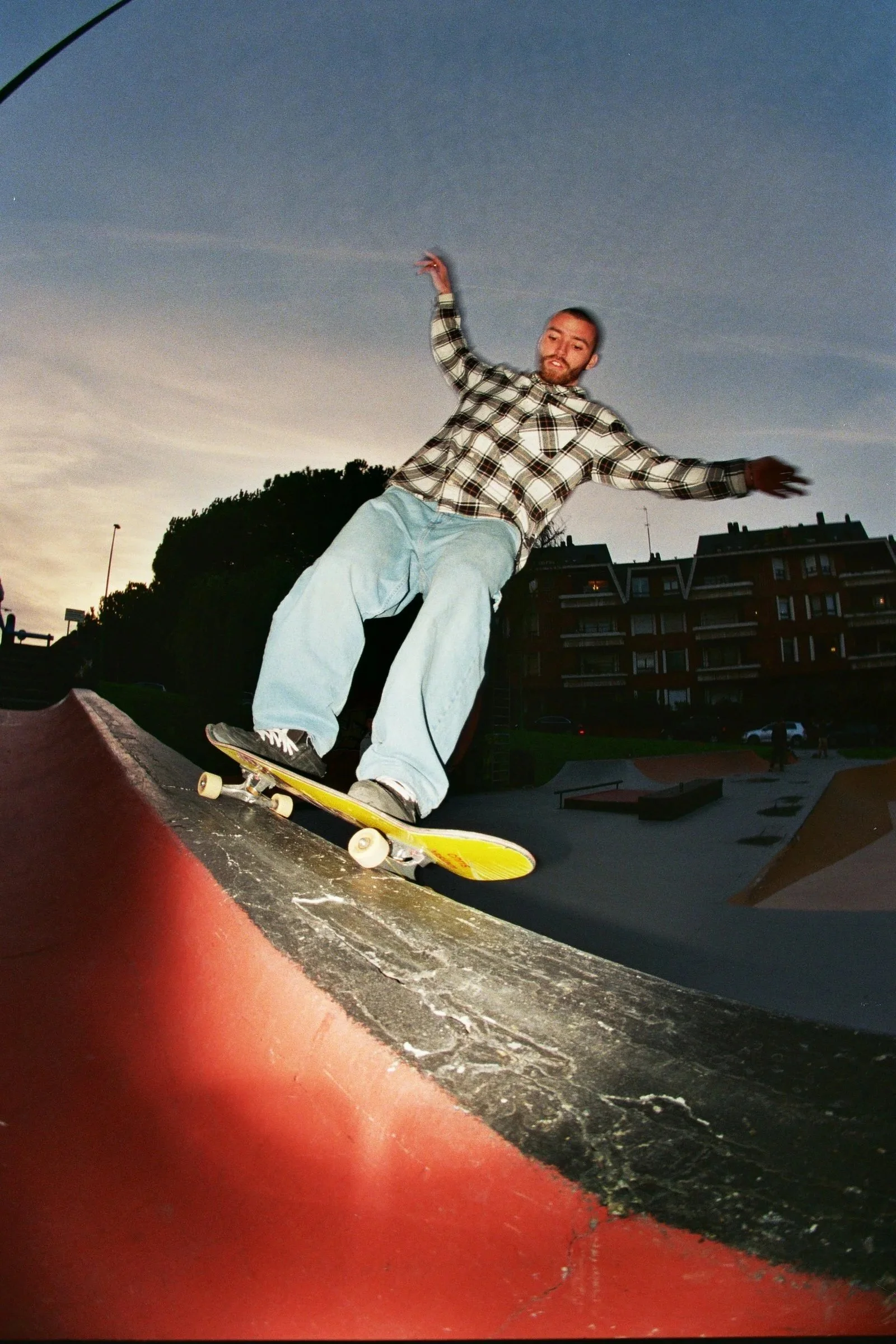 Joven patinando en un parque durante el atardecer, con edificios al fondo.