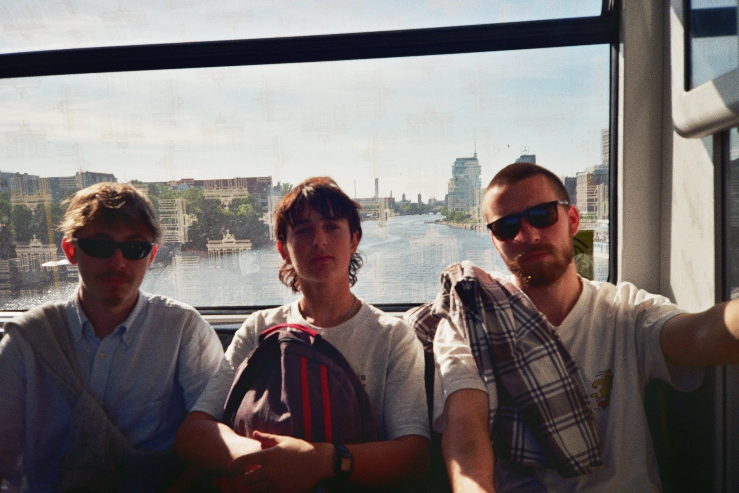 Tres jóvenes en un ferry con vista de la ciudad y río al fondo.
