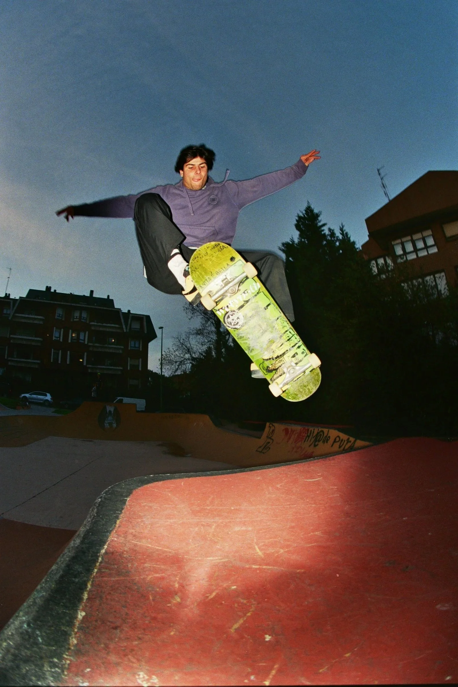 Joven haciendo un truco de skate en un parque de patinaje al atardecer.