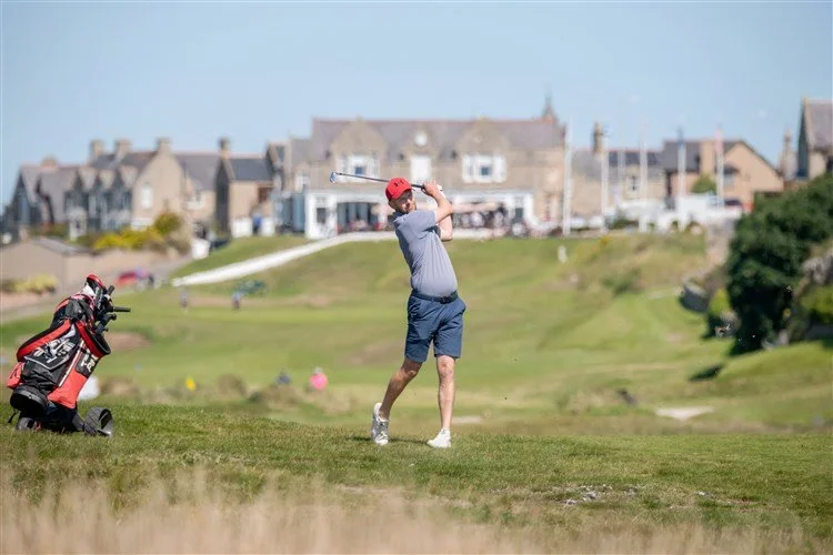 A man playing golf on a course with houses in the background and a golf bag nearby.