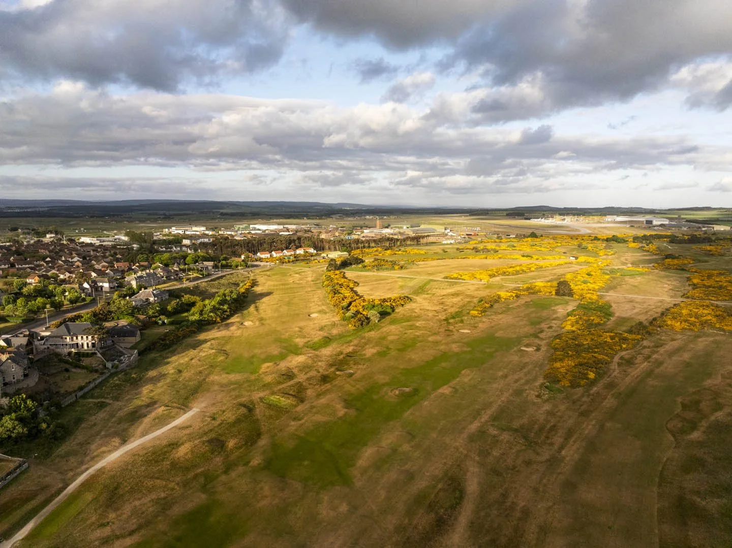 Aerial view of a suburban area with houses, a golf course, and open fields under a cloudy sky.