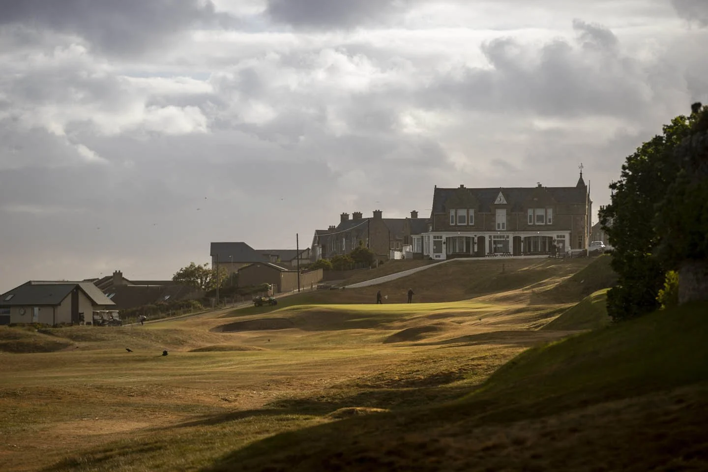 Gloomy cloudy sky above a golf course with sand traps and a large house in the background.