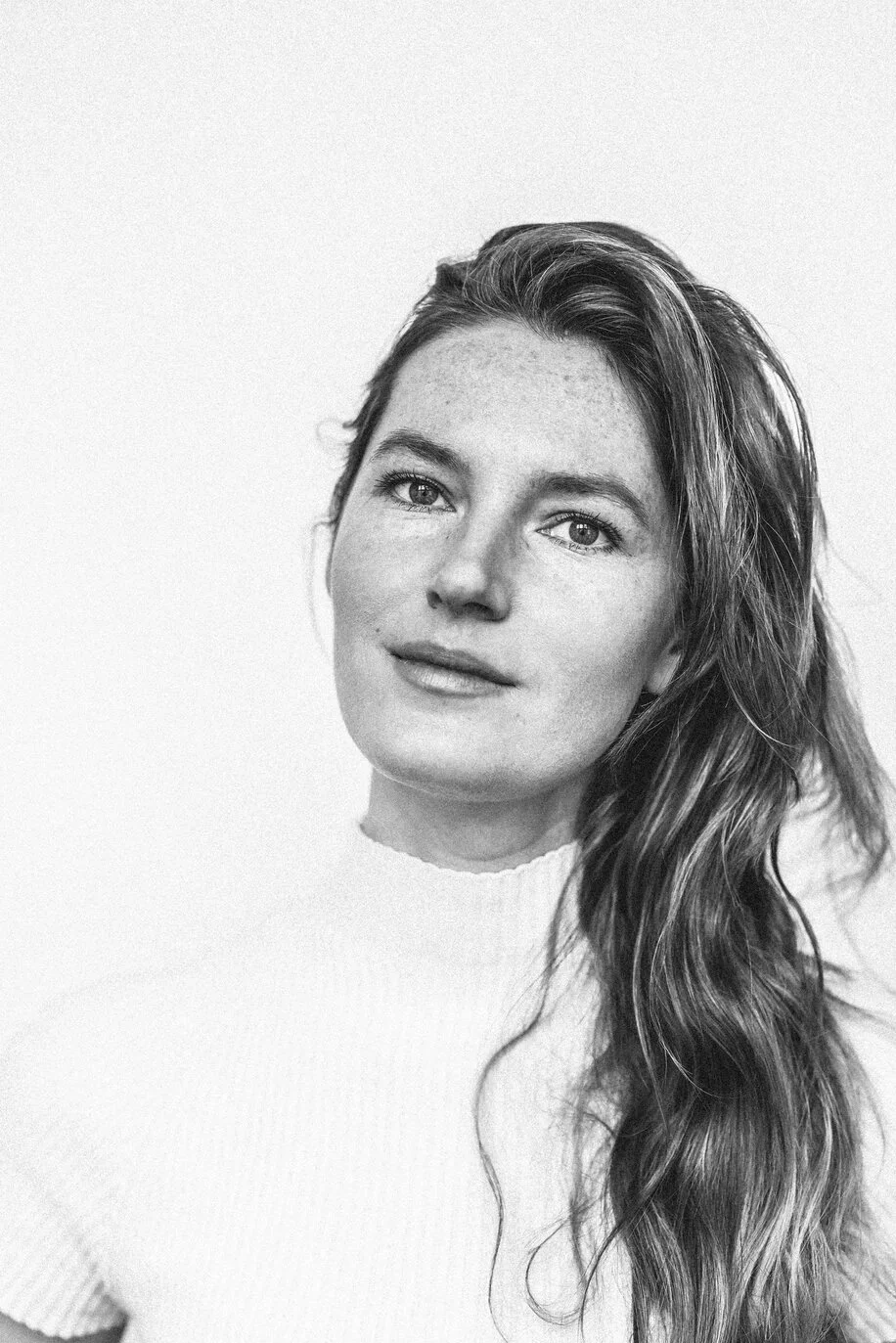 Black and white portrait of a woman with long wavy hair, smiling softly, wearing a light-colored turtleneck sweater.