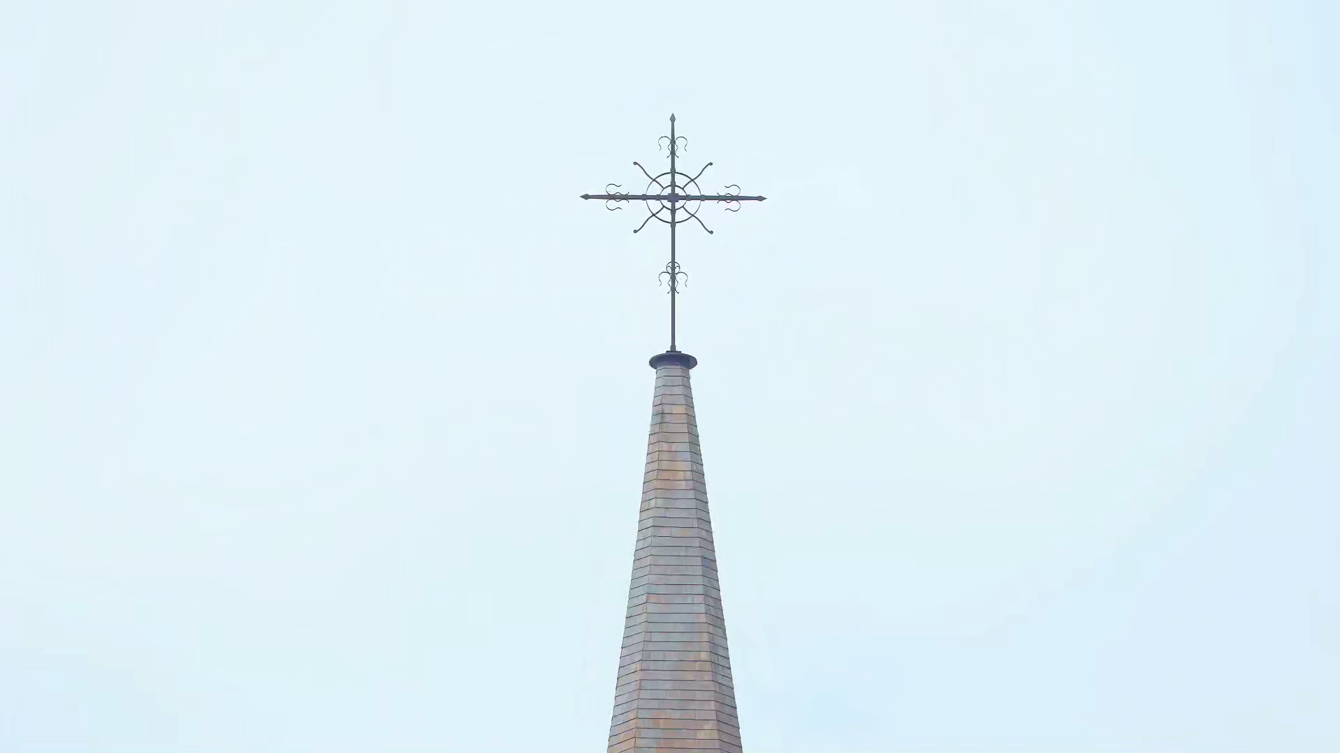 View of a church steeple with a cross at the top, set against a pale blue sky.