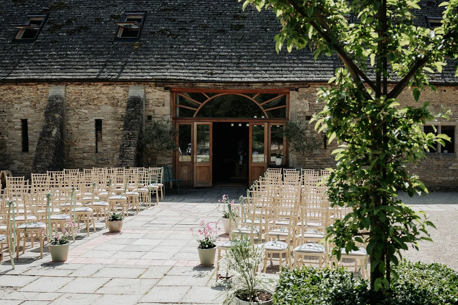 Backyard garden with string lights, benches, a small fire pit, trees, umbrellas, and a cloudy sky.