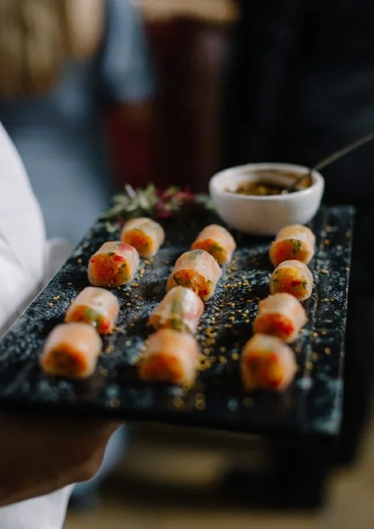 Hand holding black serving tray with sushi rolls and small bowl of dipping sauce