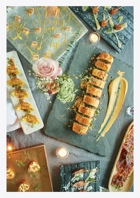 A table set with various gourmet appetizers and finger foods, including sushi, croquettes, and small bites, decorated with flowers and candles for a stylish event or party.