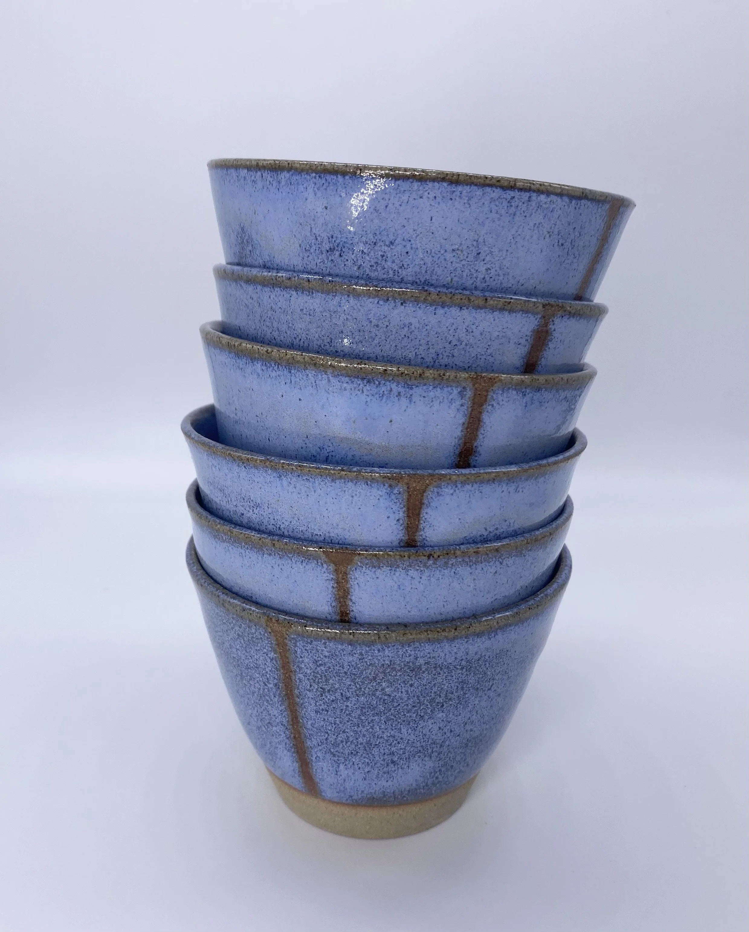 Stacked blue ceramic bowls with a mottled glaze and vertical brown lines on a white background.