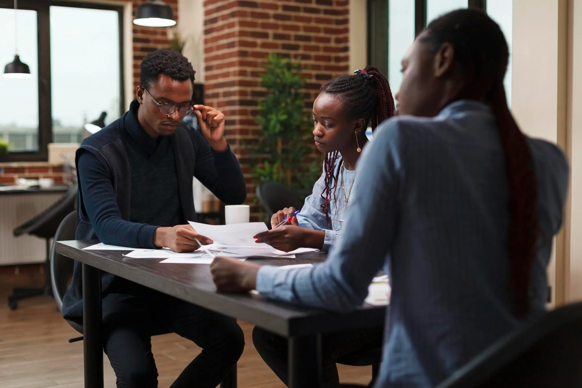 Three diverse individuals sitting at a table in a modern office, reviewing documents during a meeting.