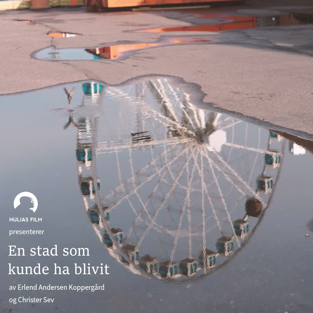 Refleksjon av et par hjul på vannansamling på en asfaltvei, med en bystruktur i bakgrunnen.