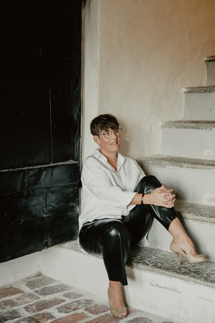 Person som sitter på en trappa, har på sig vit skjorta, svarta byxor och högklackade skor.