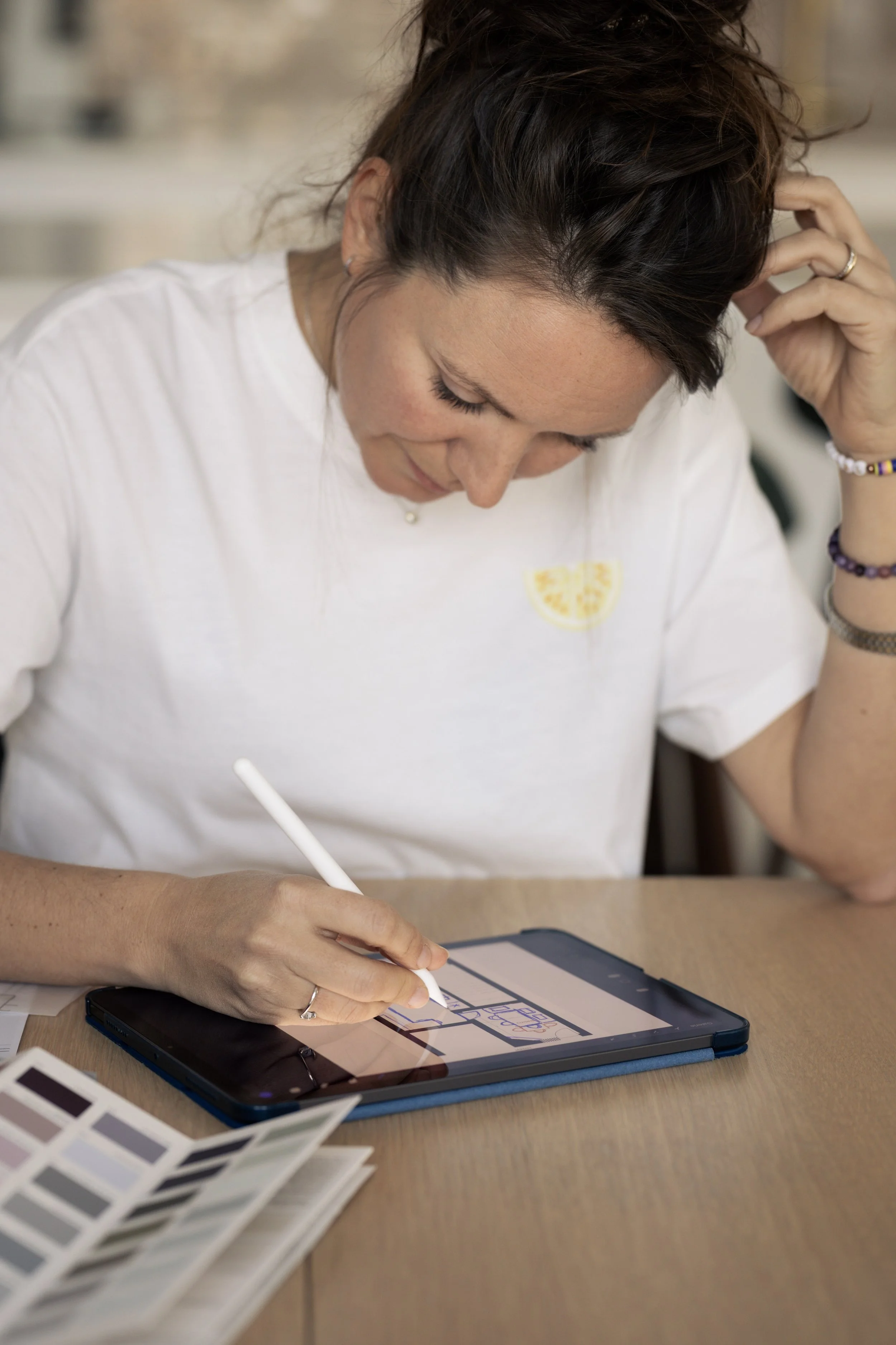 Une femme utilise une tablette avec un stylet, il y a un nuancier de couleurs sur la table.