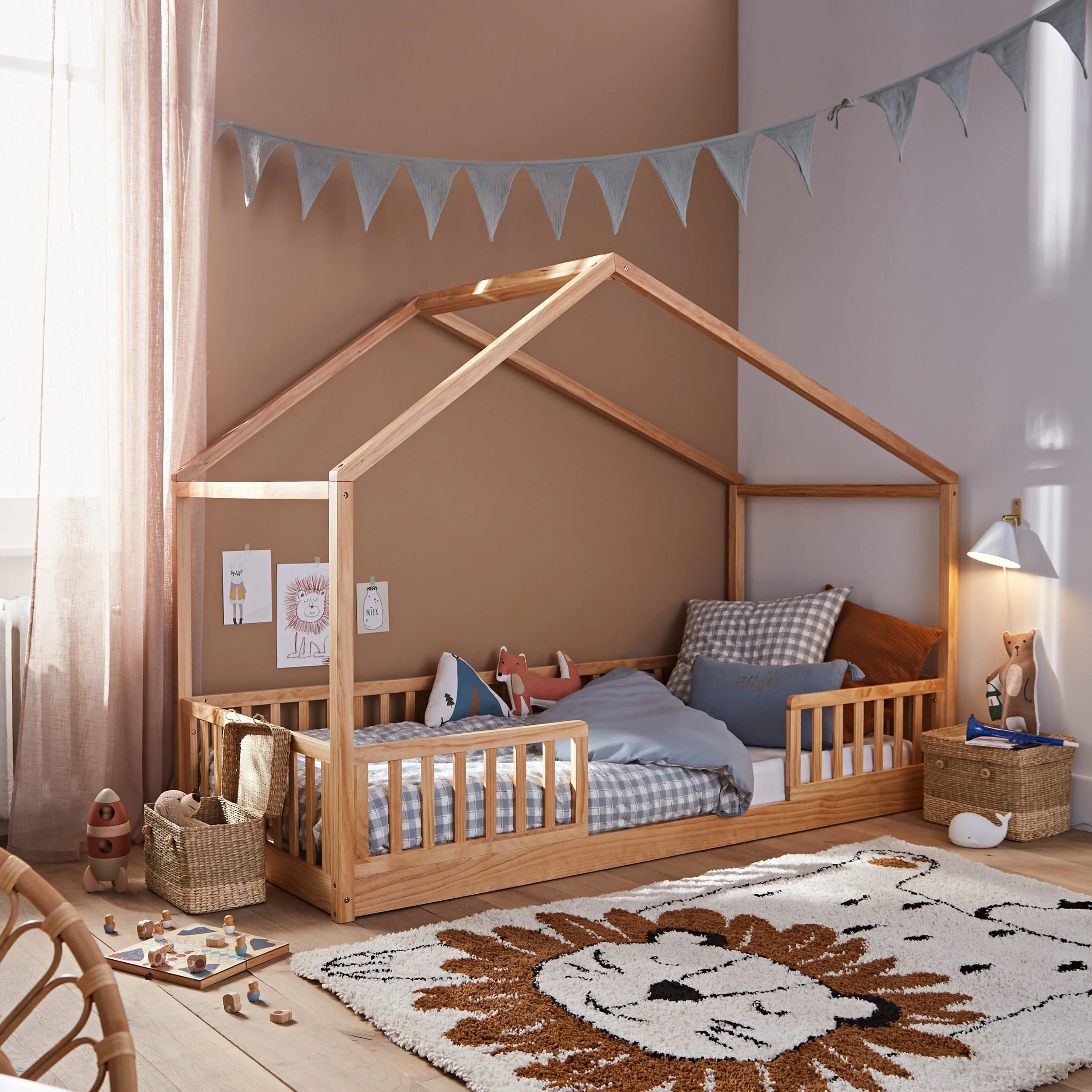 Chambre d'enfant avec cadre de lit en forme de maison en bois, décorée avec des poupées et des dessins, tapis en forme de lion, et jouets en bois.