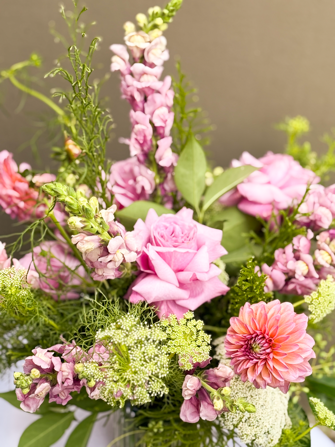 A bouquet of pink roses, dahlias, and snapdragons with green leaves and filler flowers.