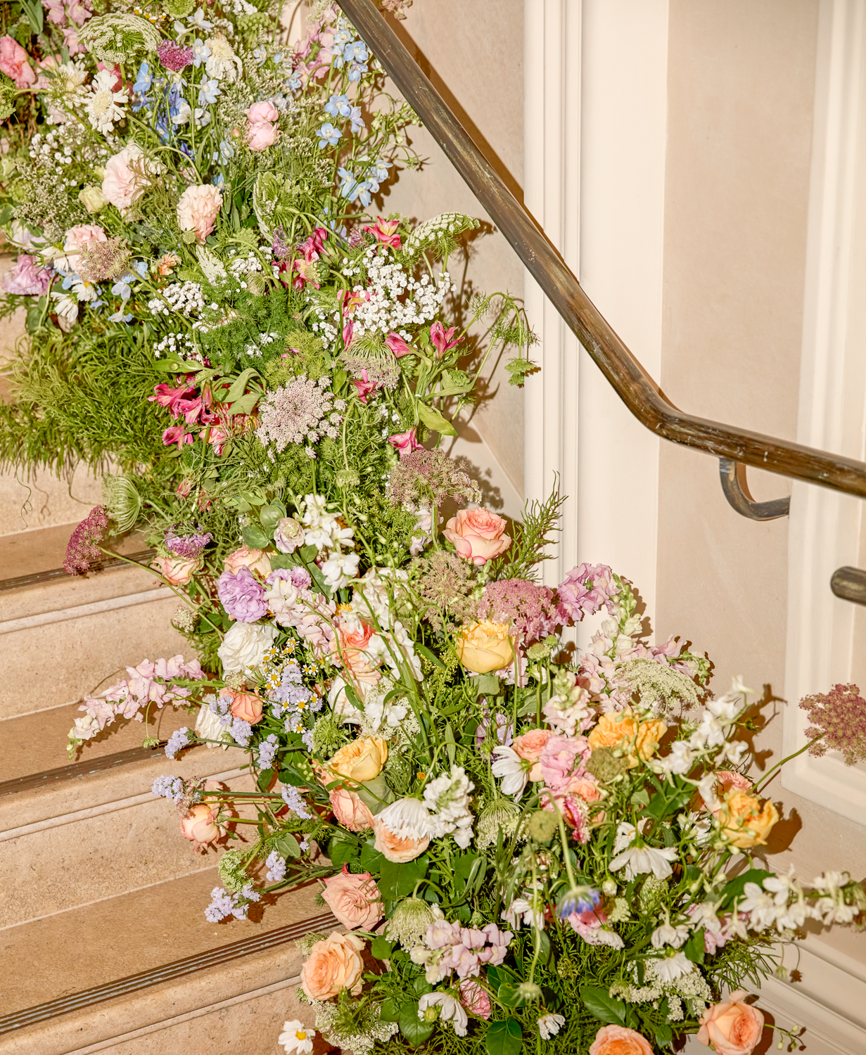 A staircase decorated with colorful flowers, including roses, daisies, and other blossoms, along a handrail on the right side.