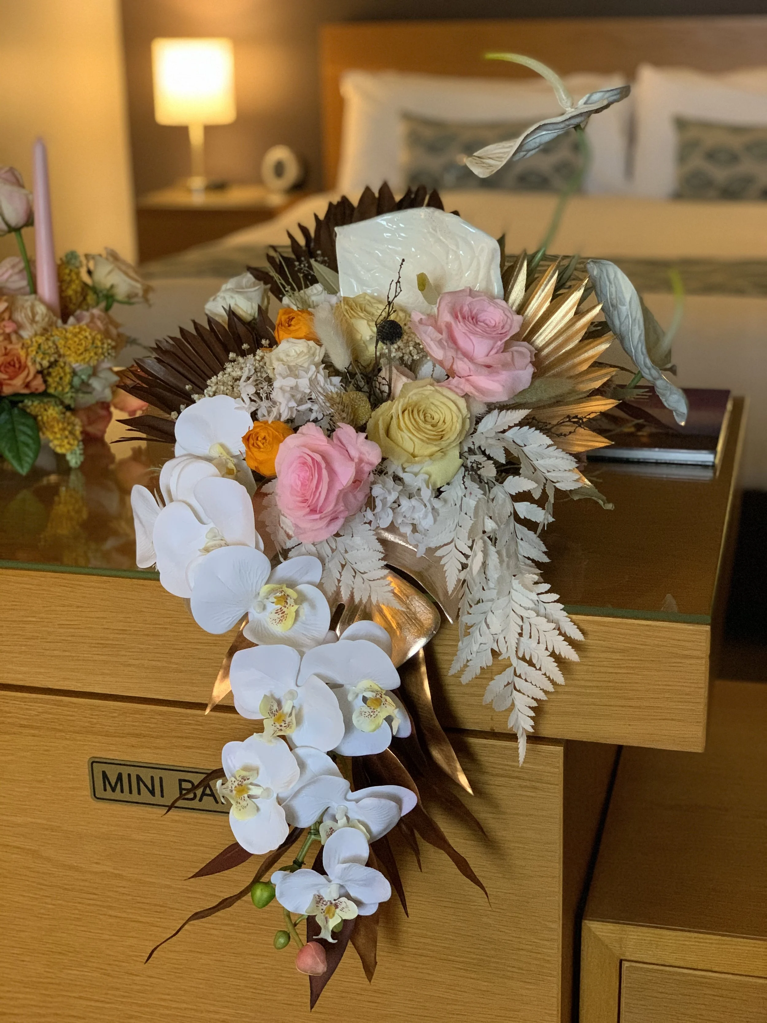 A floral arrangement with white orchids, pink roses, yellow roses, and other flowers on a wooden table.