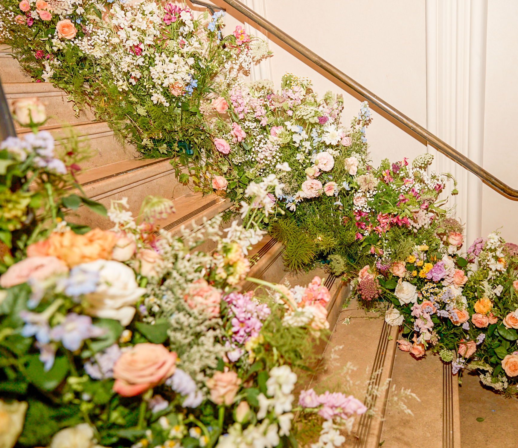 A staircase decorated with an abundance of colorful flowers, including roses, daisies, and other blooms, creating a floral display on the steps and surrounding area.
