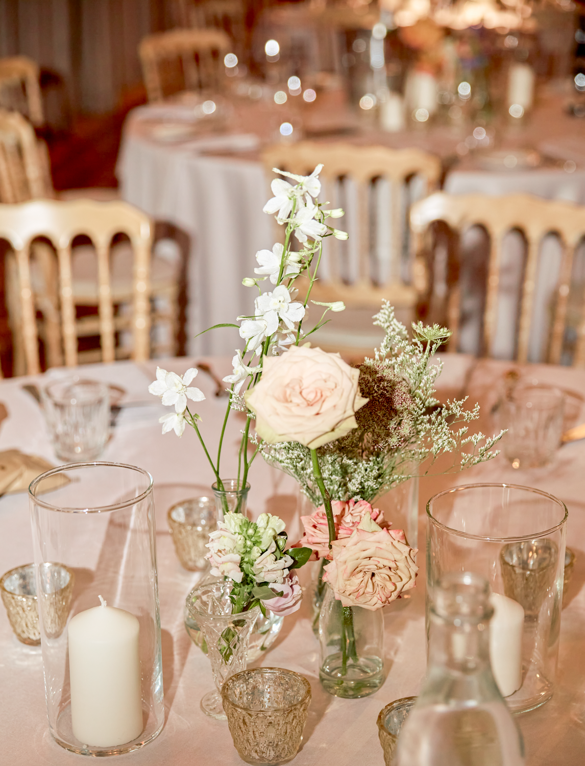 Elegant table centerpiece with white and blush flowers, surrounded by candles and glassware at a formal event.