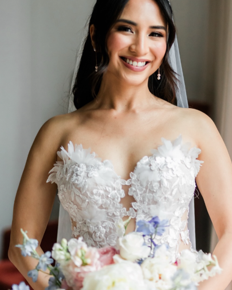 A smiling bride in a white lace wedding dress holding a bouquet of flowers.