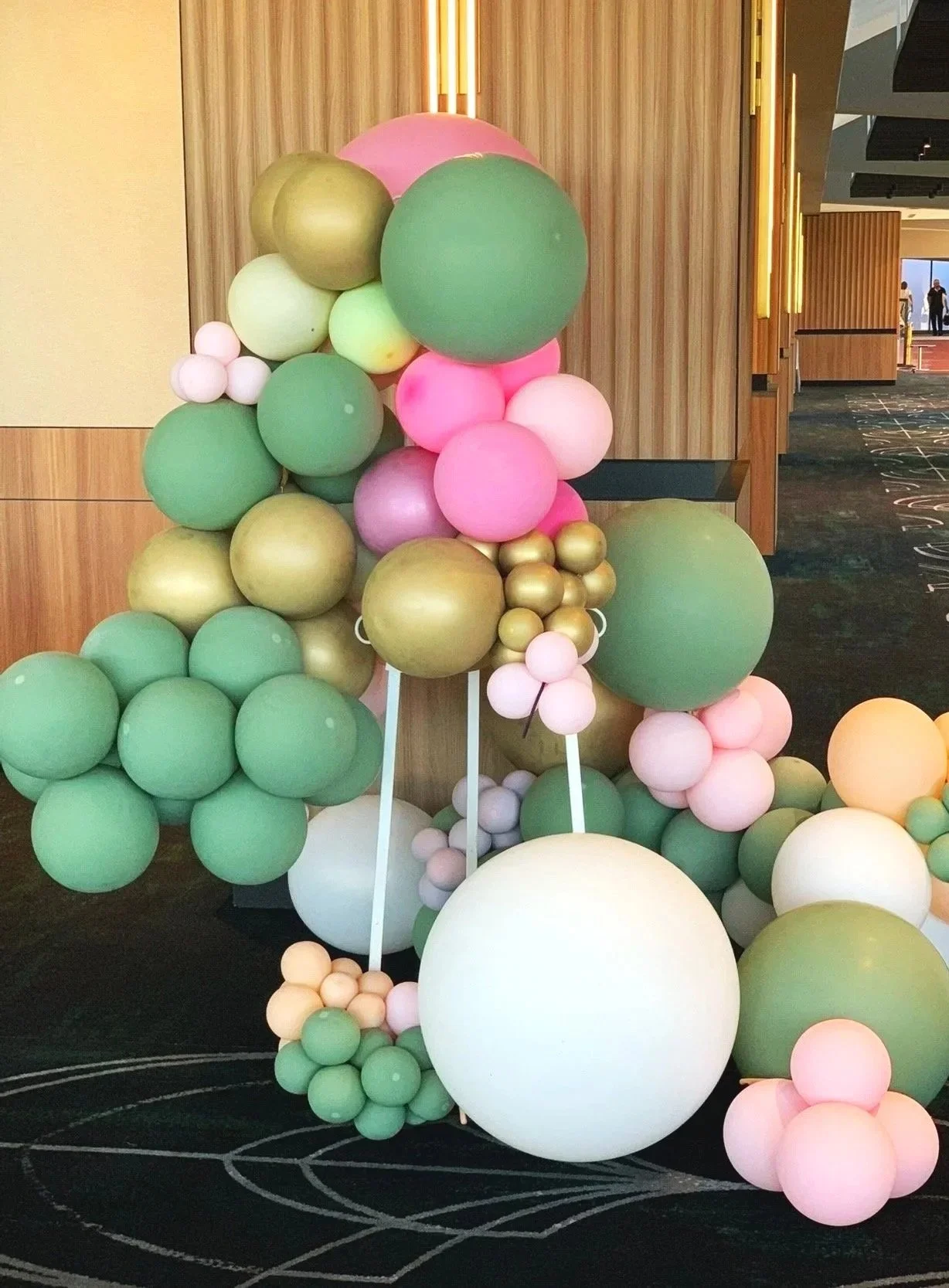 Decorative arrangement of pastel green, pink, gold, and white balloons in a modern indoor setting.