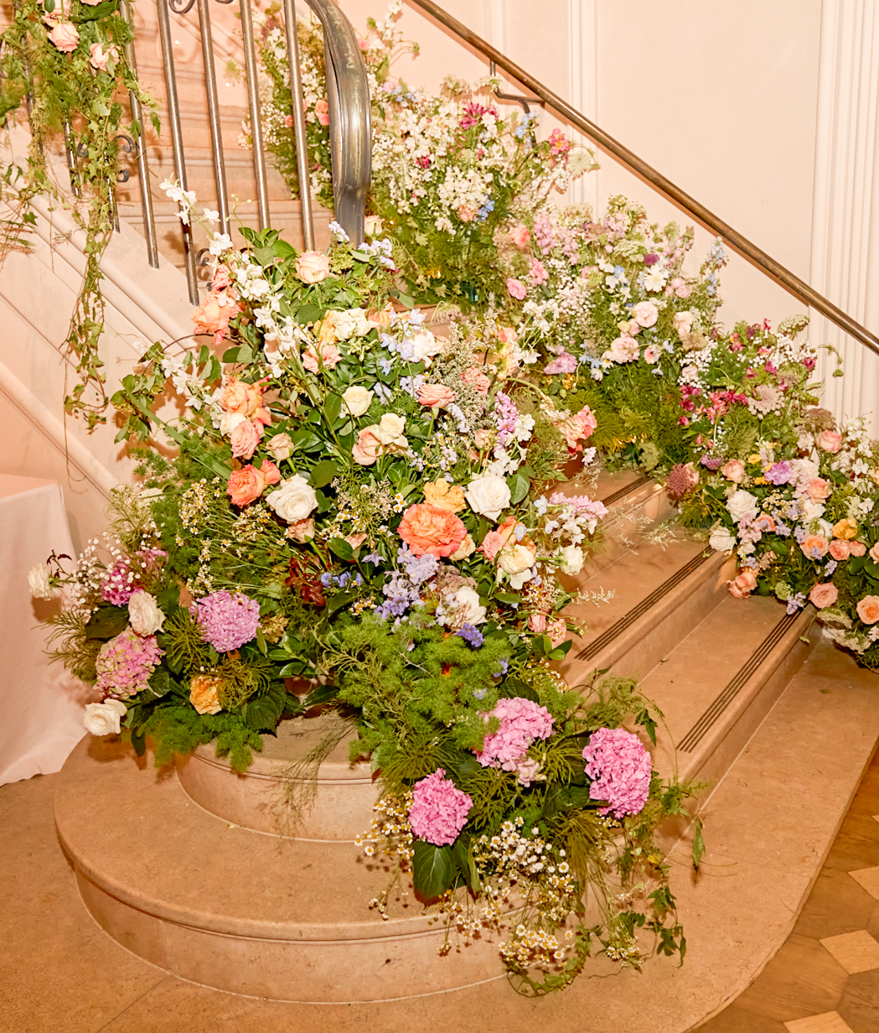 An elaborate floral arrangement of pink, white, purple, and peach flowers is displayed on a staircase, decorating the steps and railing.
