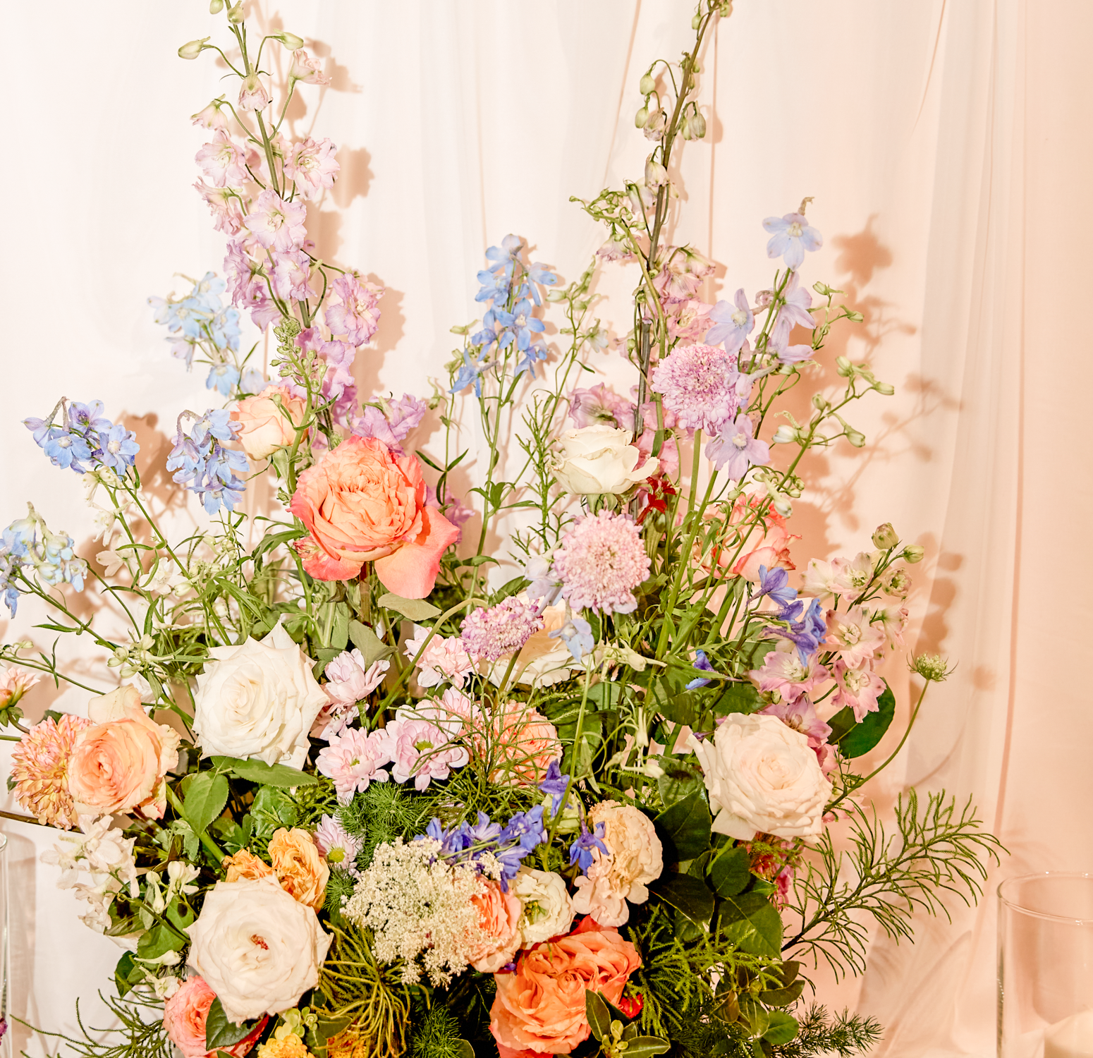 A floral arrangement with pink, white, peach, and blue flowers against a light-colored backdrop.