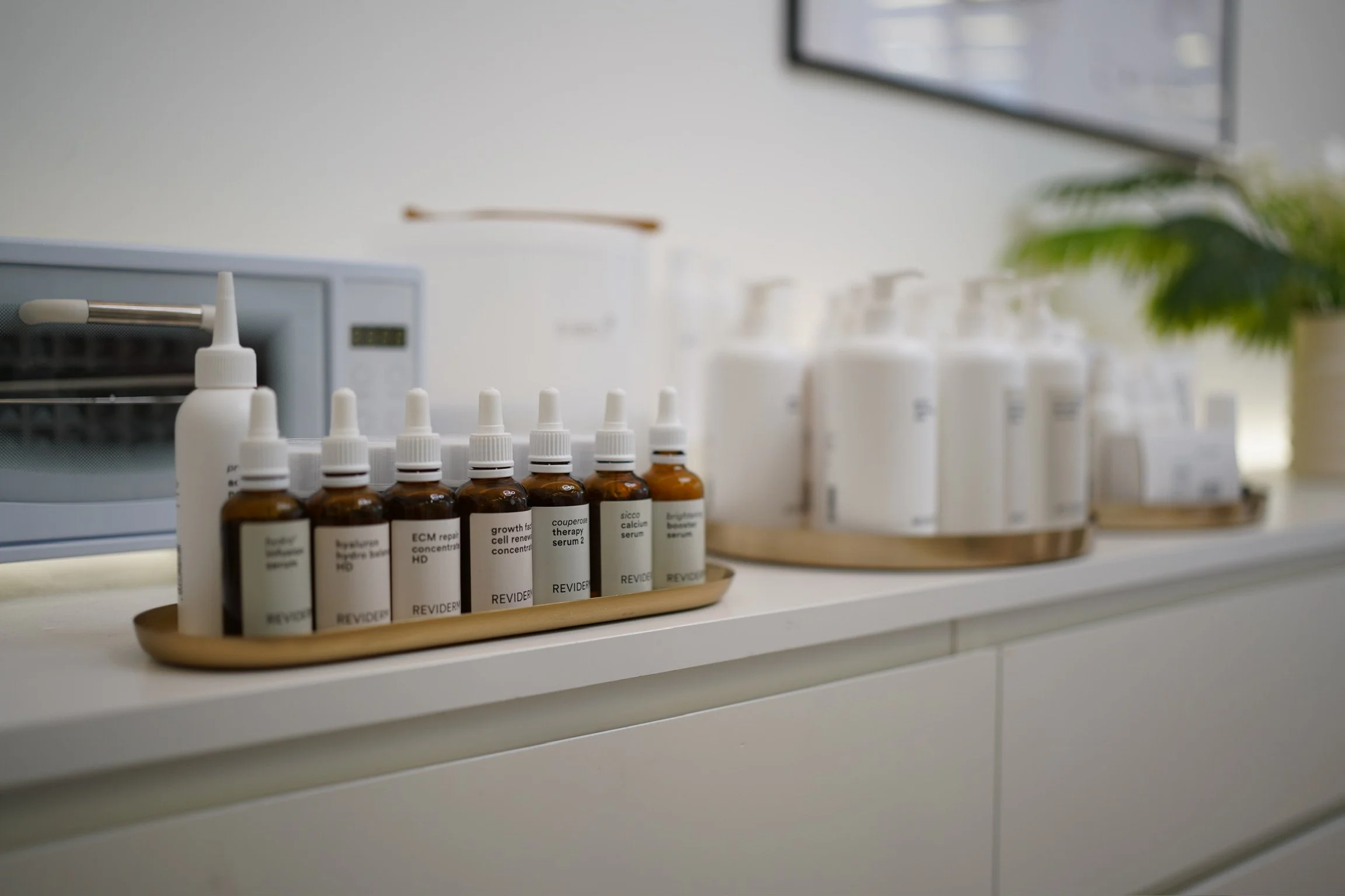 Medizinische Fläschchen in einem Beistellteller auf einer weißen Oberfläche, im Hintergrund ein Autoklav und eine Pflanze.