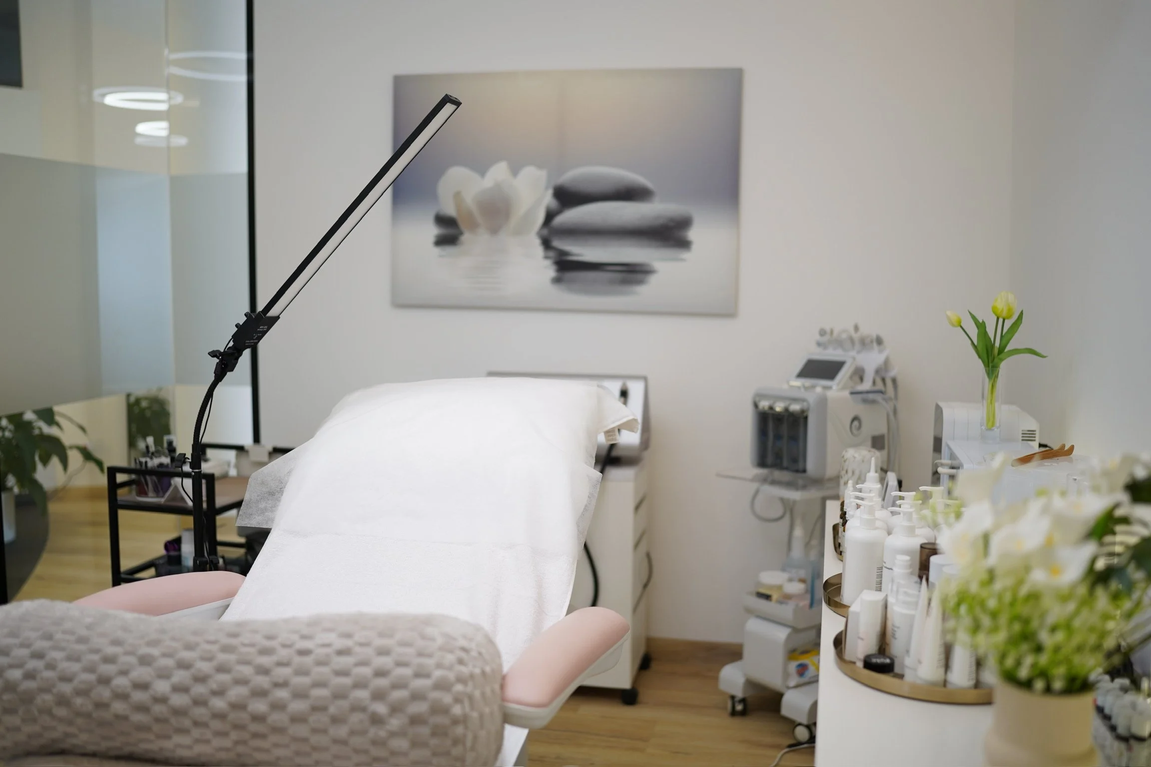 Behandlungsraum in einer Schönheitsklinik mit Behandlungsbett, medizinischen Geräten, Pflegeprodukten und Dekoration mit Tulpen