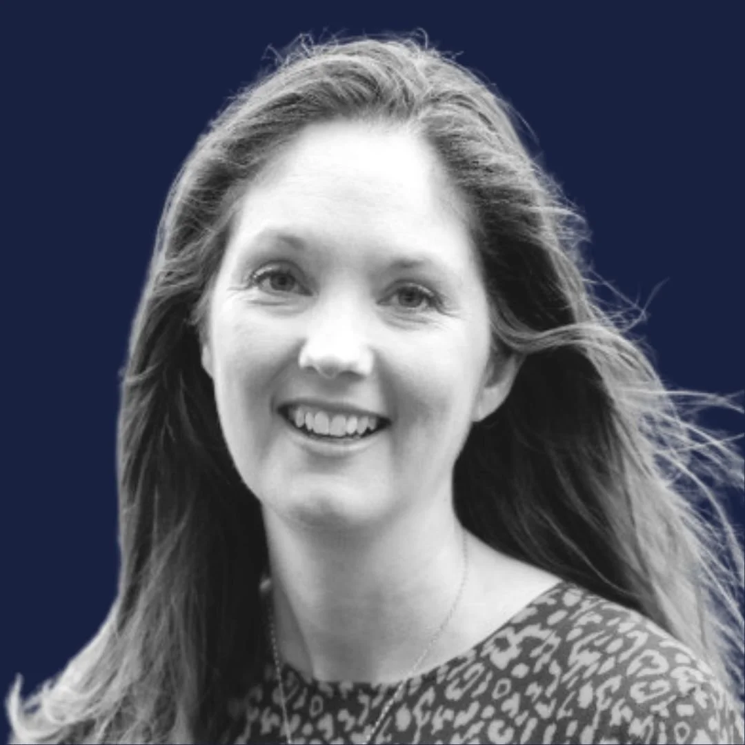 Black and white portrait of smiling woman with long hair wearing a patterned top, against a dark background.