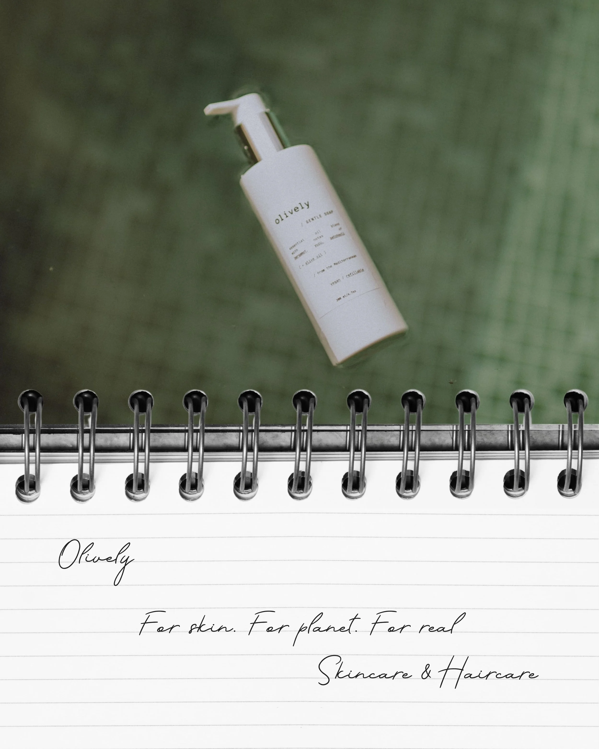 Un frasco de producto de cuidado de la piel llamado Olively flotando en un fondo verde con una libreta en primer plano que tiene el texto: "Olively. For skin. For planet. For real. Skincare & Haircare."