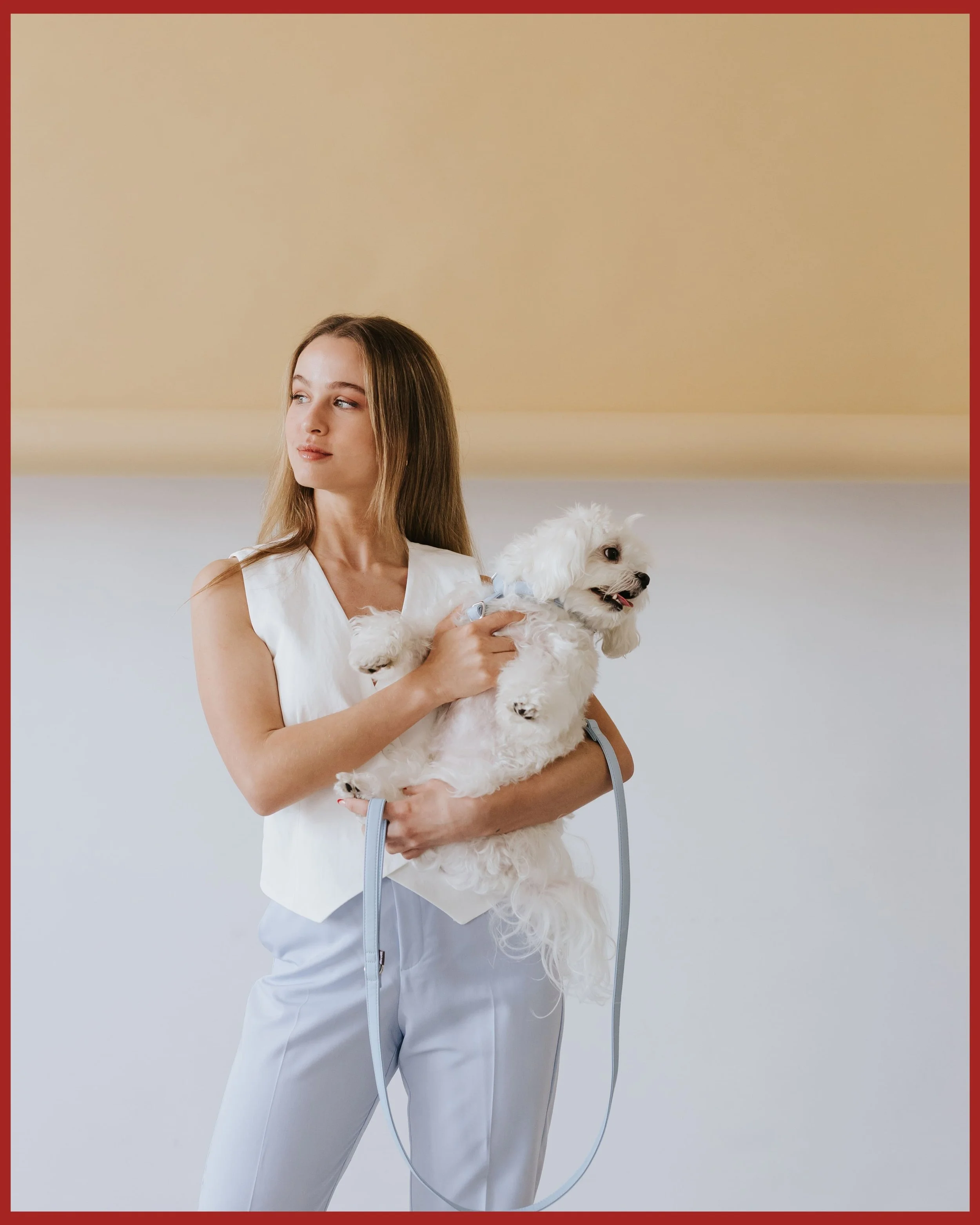 Mujer joven sosteniendo un perro blanco pequeño en un ambiente interior para el shooting de la marca Brott Barcelona de accesorios para perros