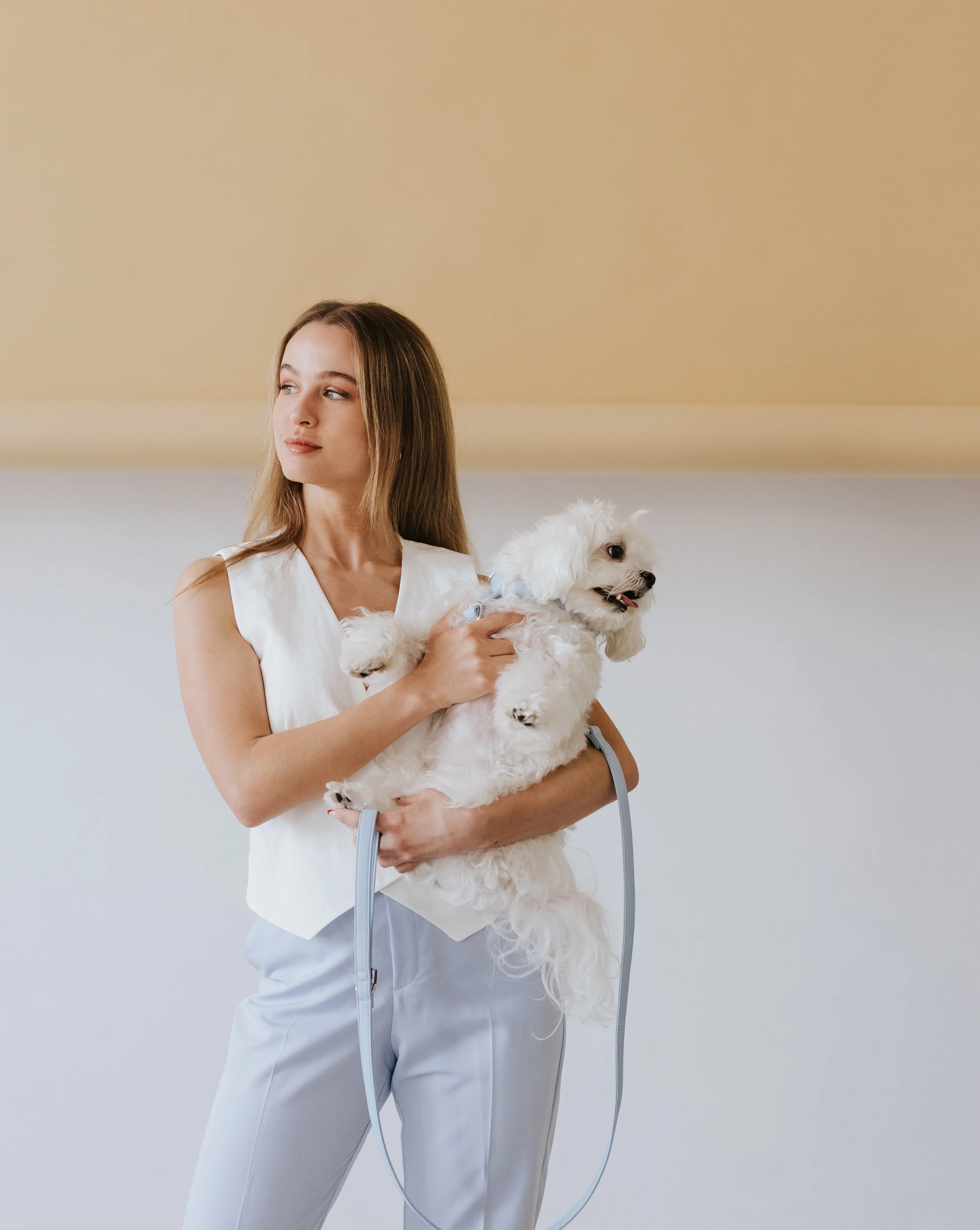 Mujer joven con ropa blanca sosteniendo un perro pequeño blanco con pelaje rizado.