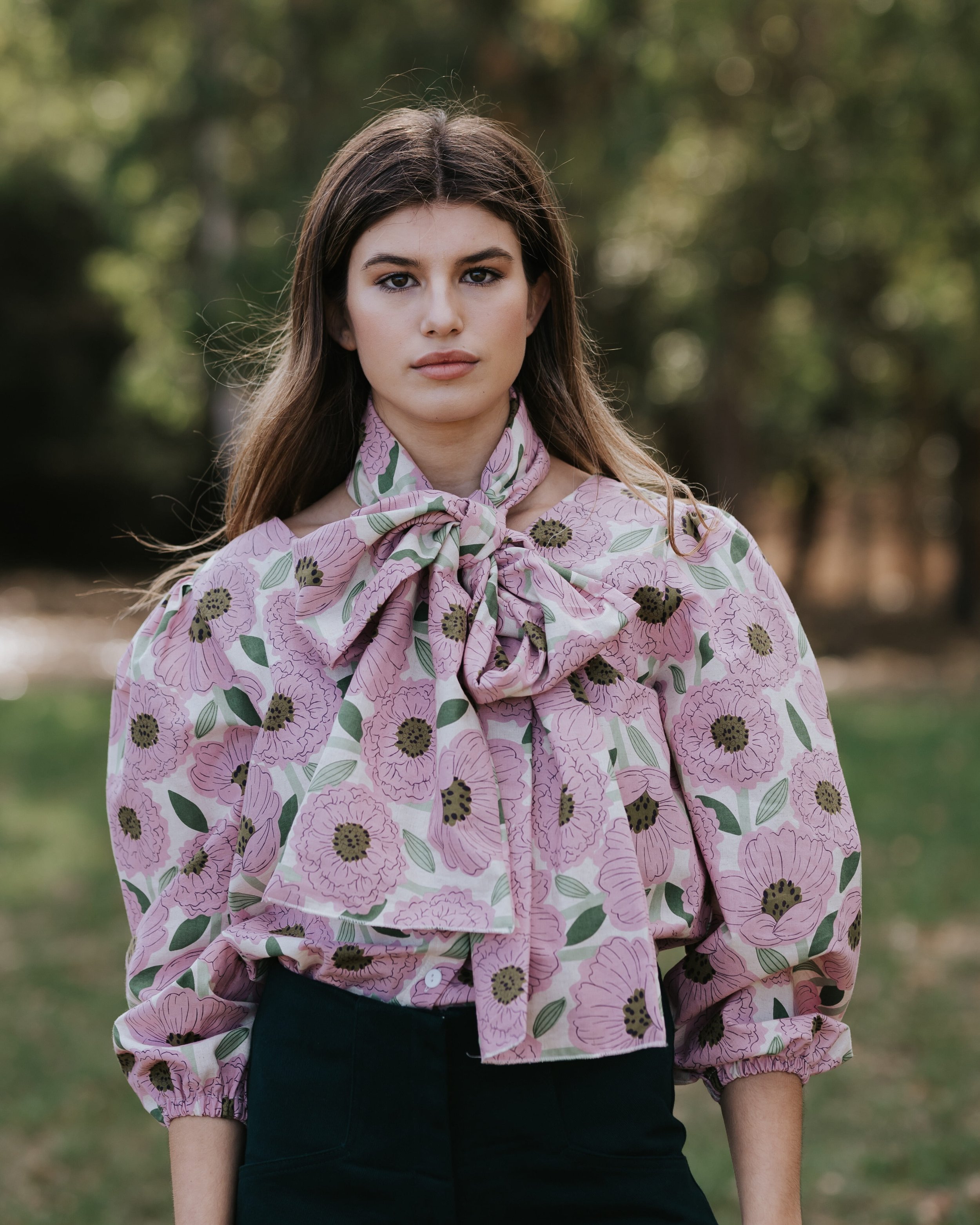 Joven mujer en exteriores con blusa de flores rosa y lazo en el cuello.