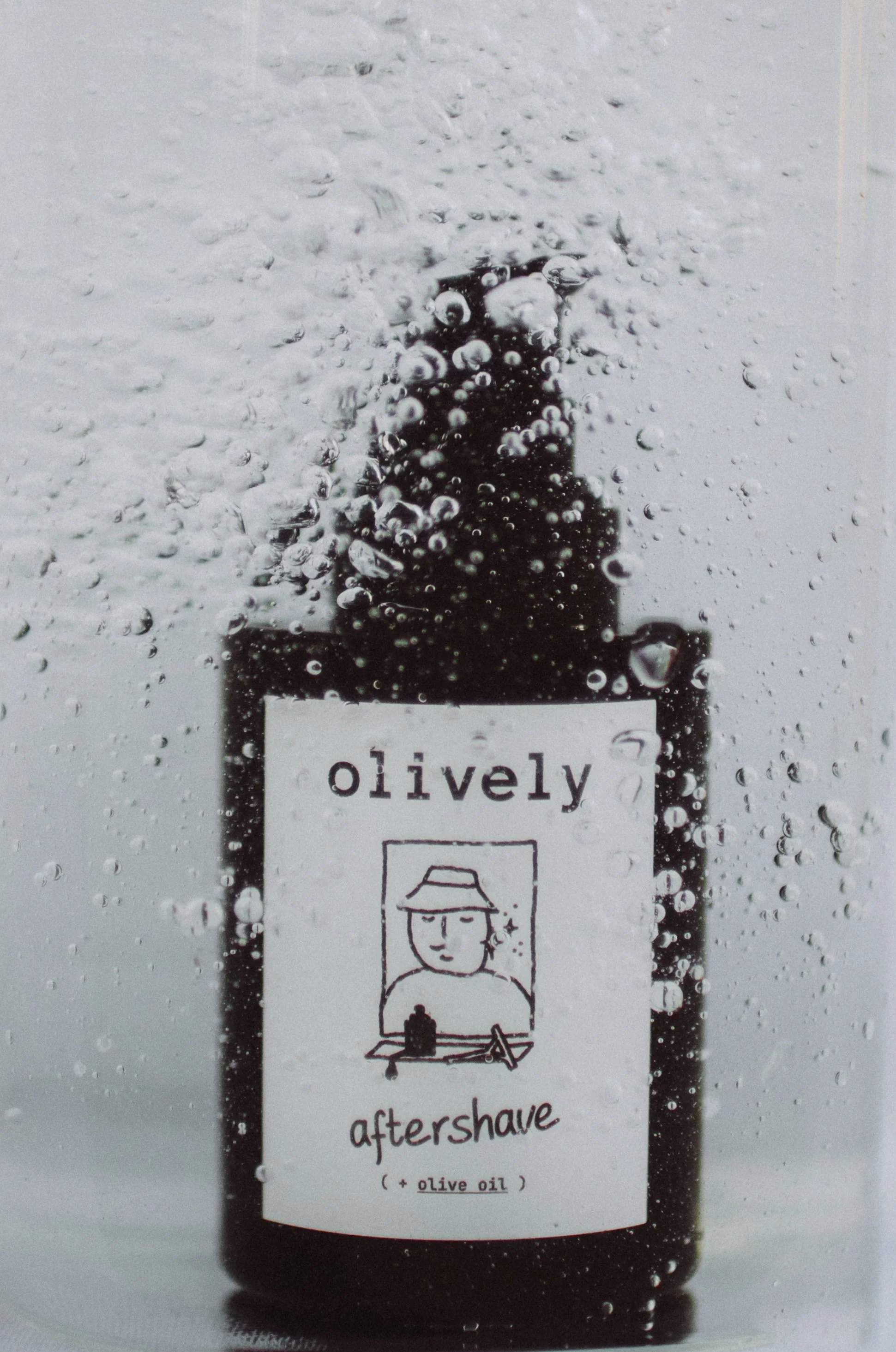 Botella de aceite de oliva para afeitado después, con burbujas y gotas de agua en la superficie.