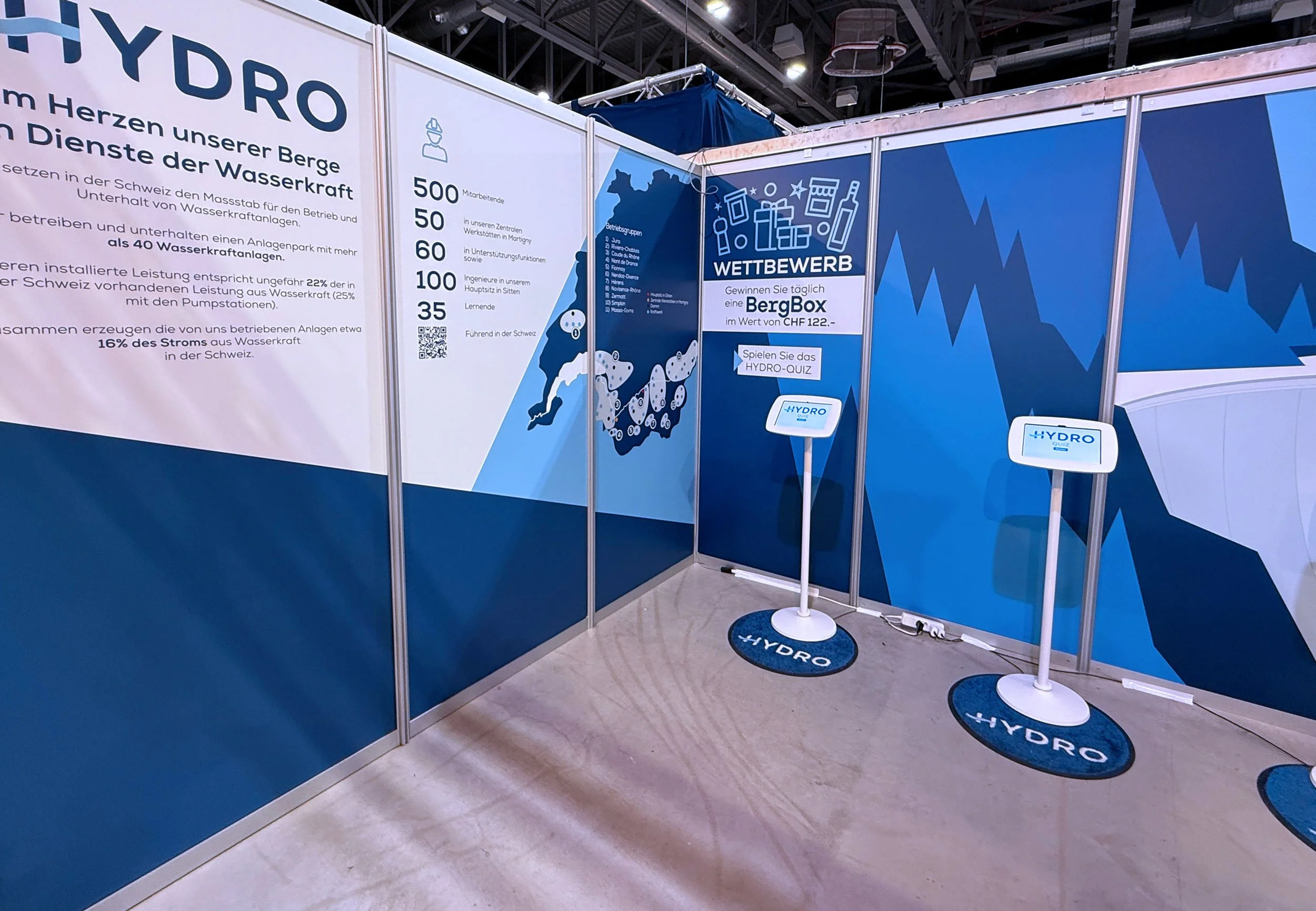 Une photo d'un stand lors d'une foire pour les entreprises. Les parois du stand sont brandé et design avec des illustrations vectoriels de couleur bleus.