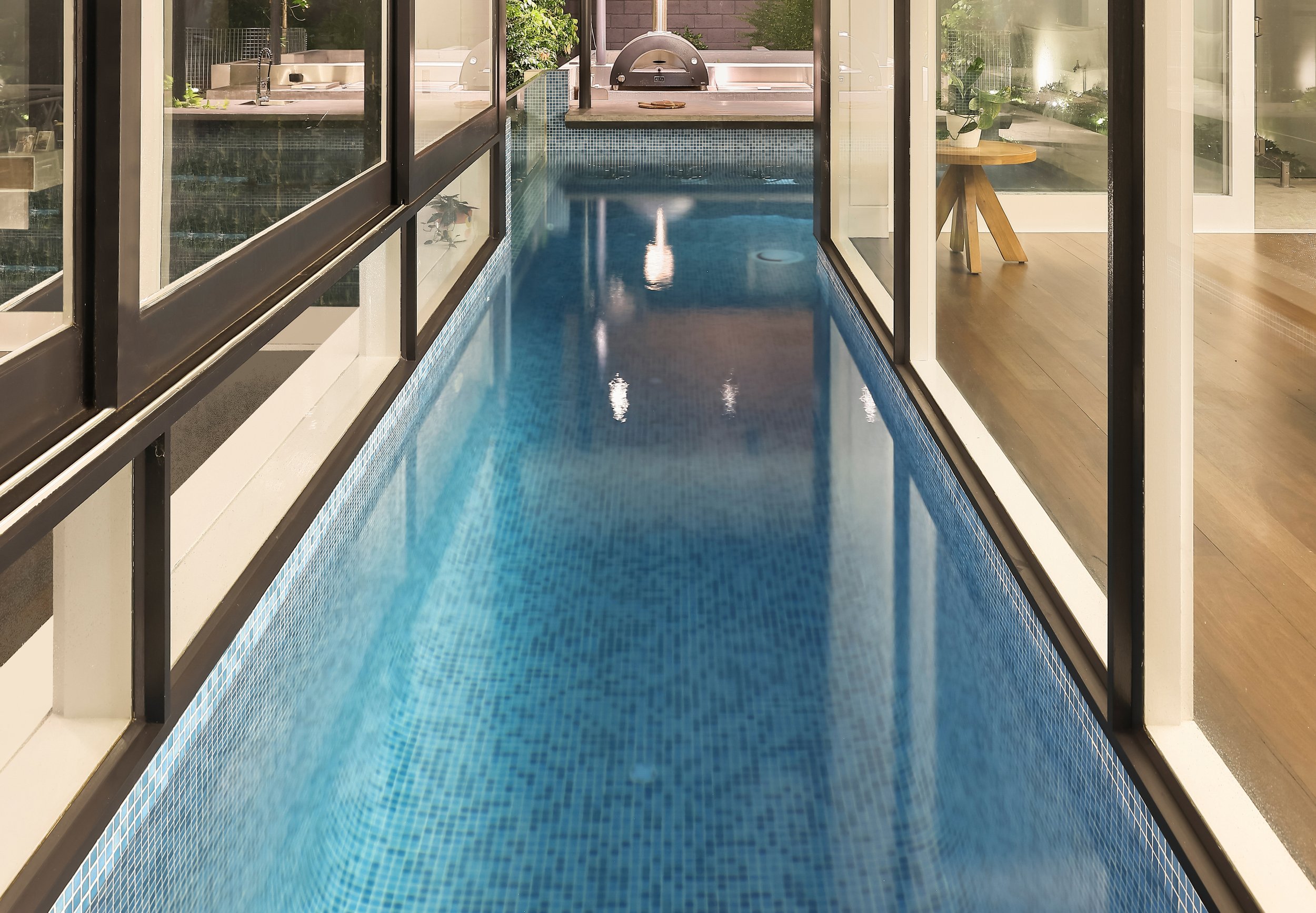 Indoor swimming pool with blue mosaic tiles, enclosed by glass walls build by Reef Pools Cronulla