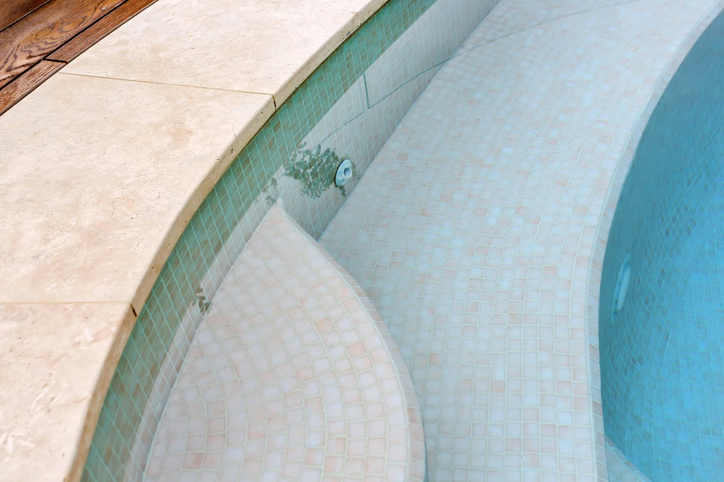 Close-up of the swimming pool with a tiled interior and a beige stone and wood deck surrounding it.