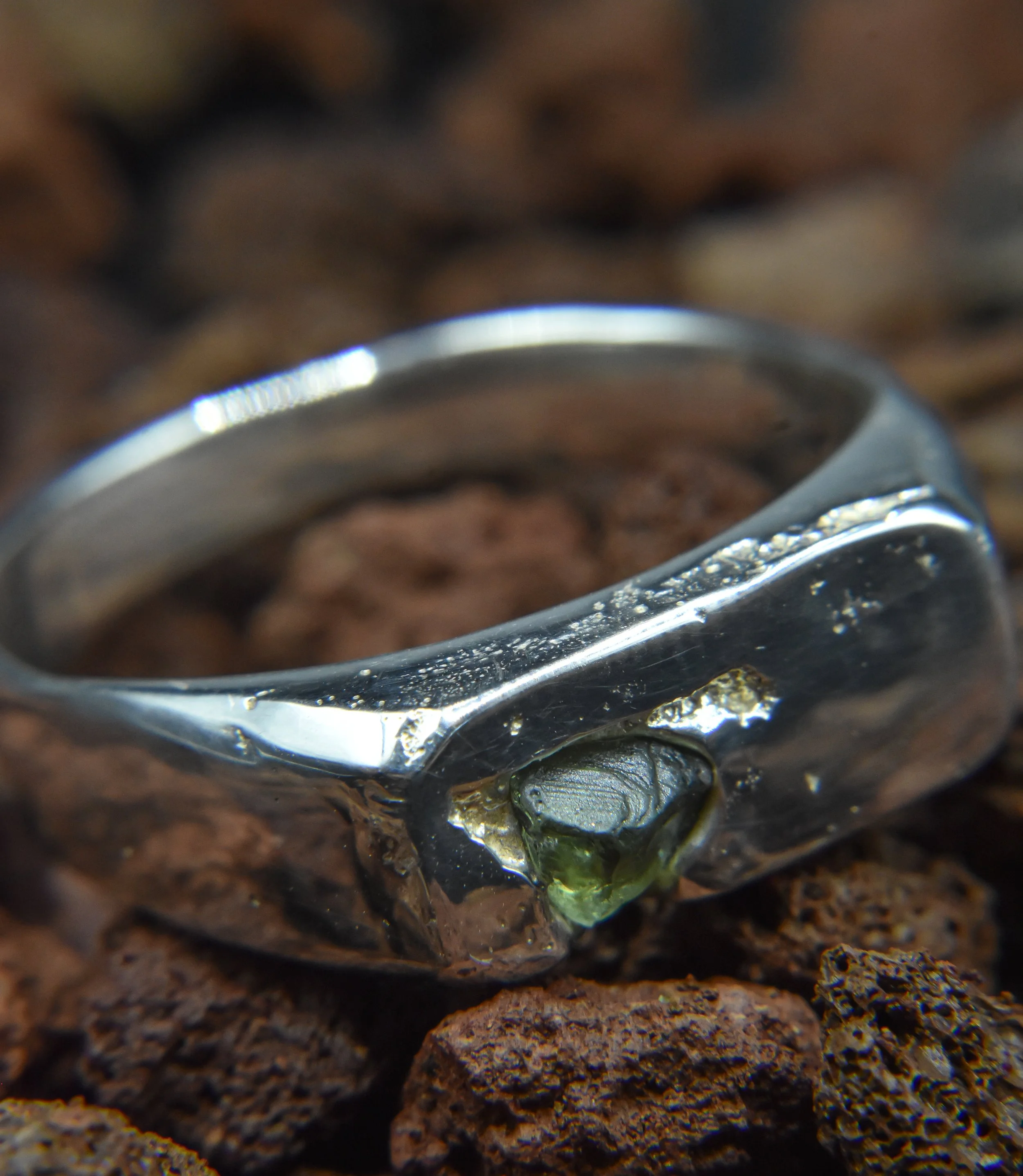 A close-up of a silver ring with a small gemstone, placed on rough brown rocks.