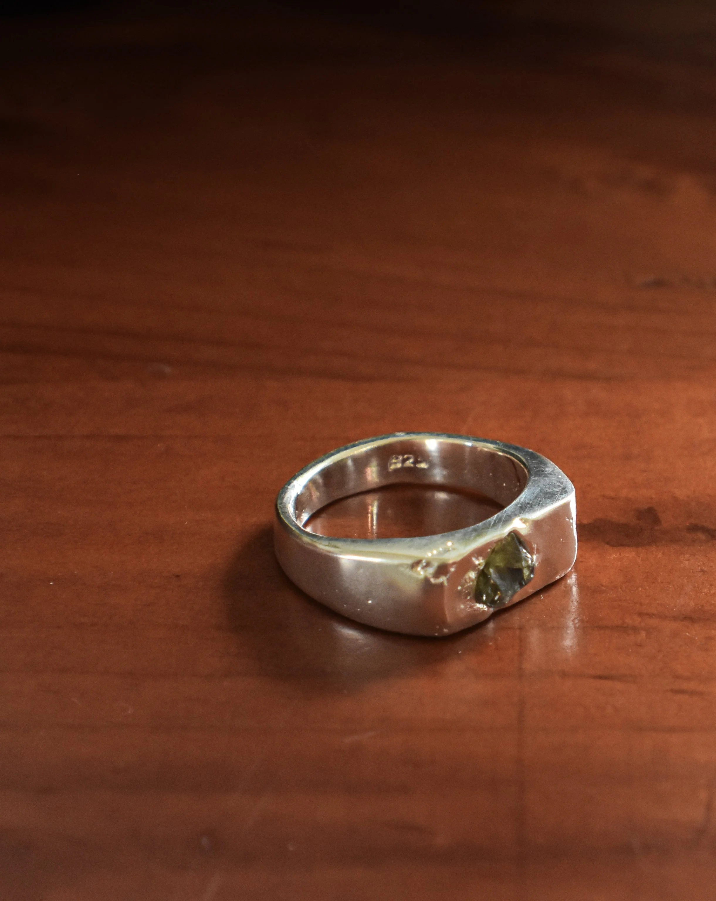 Silver ring with a dark-colored gemstone on a wooden surface.