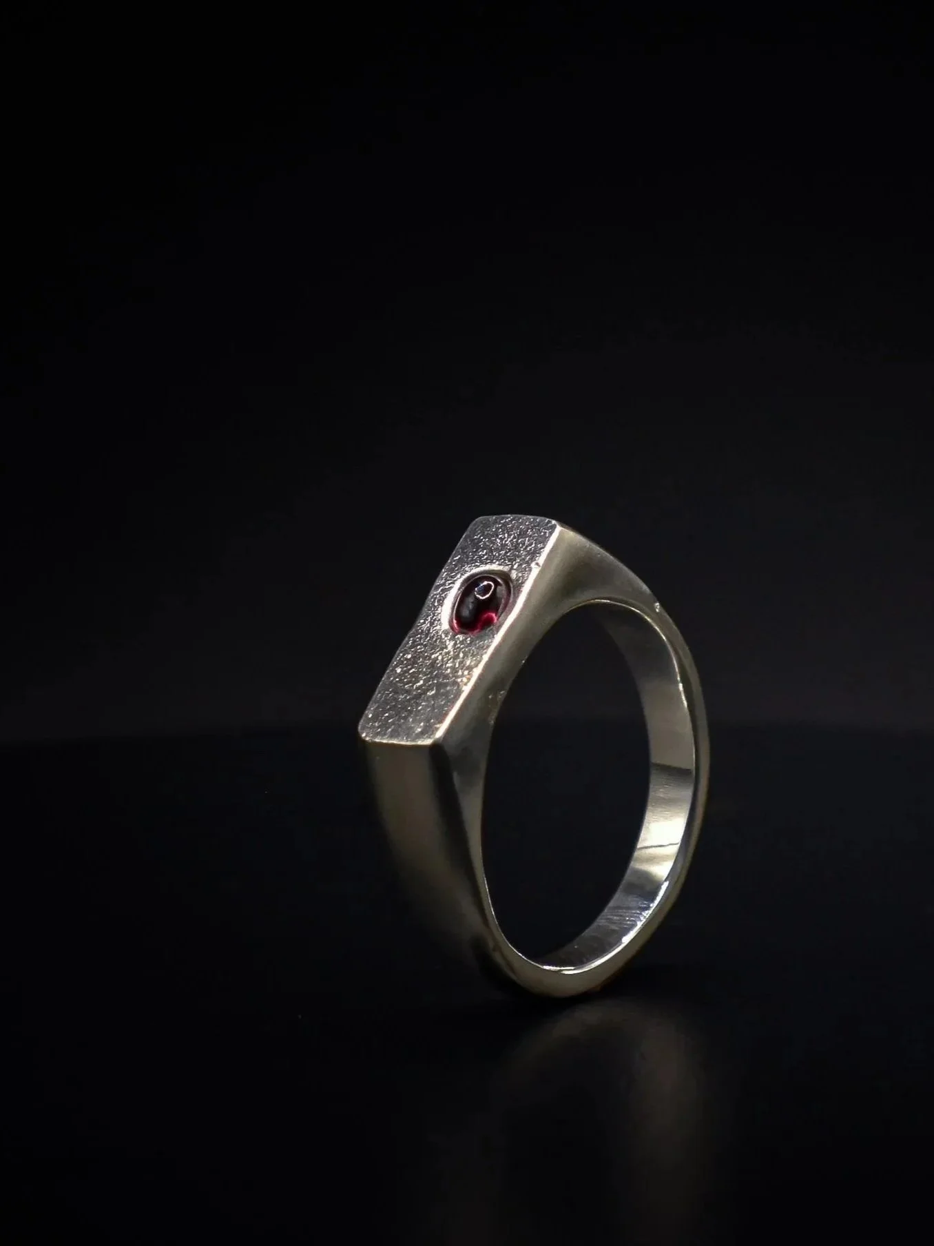 A silver ring with a black and red gemstone set on a dark background.